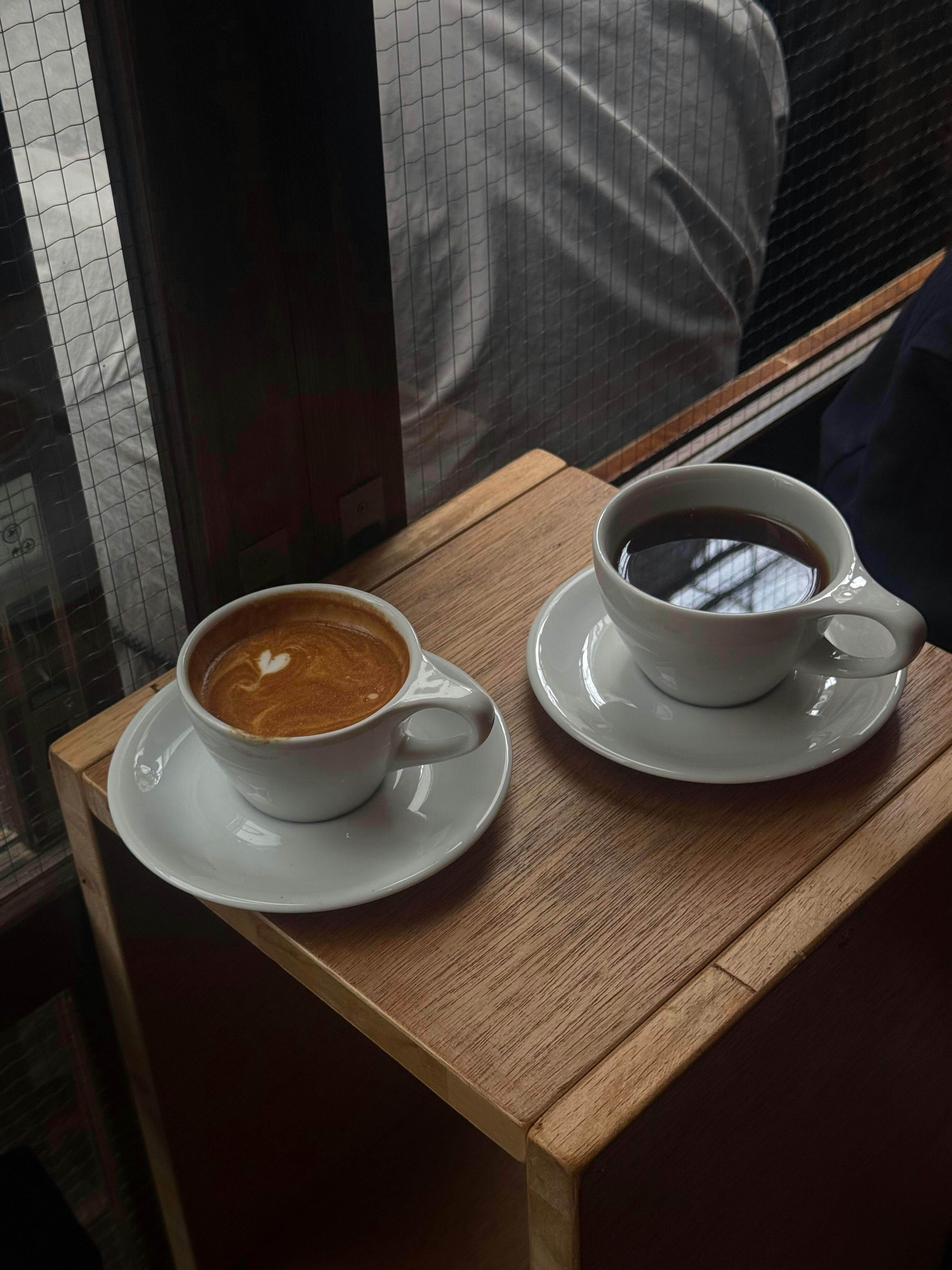 Deux tasses de café, espresso et noir, sur une table en bois.