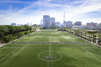 Multiple soccer fields with a modern city skyline backdrop.
