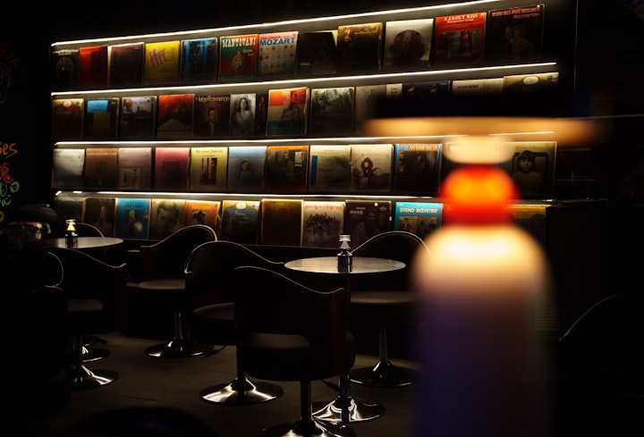 Dimly lit bar with an illuminated vinyl record collection, photo by X F on Unsplash