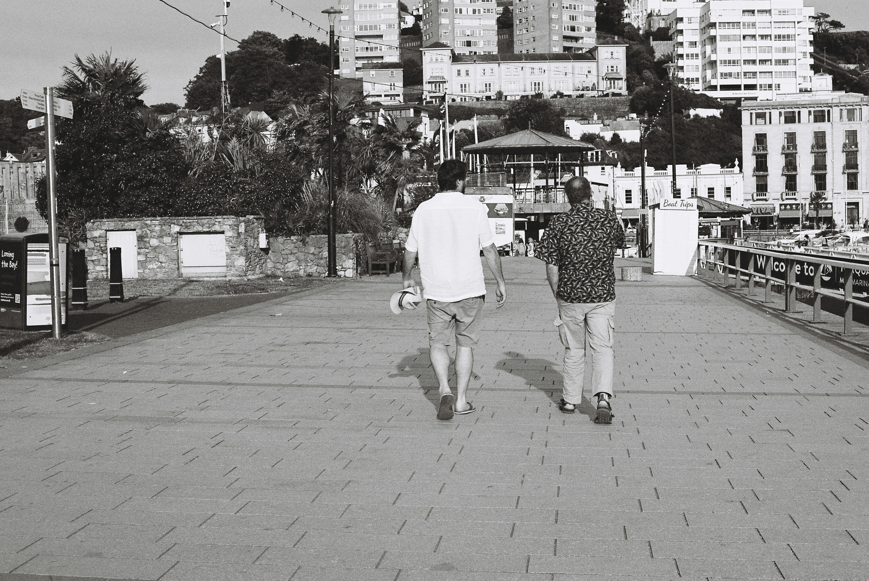Dos hombres caminan por un camino pavimentado con edificios de la ciudad.