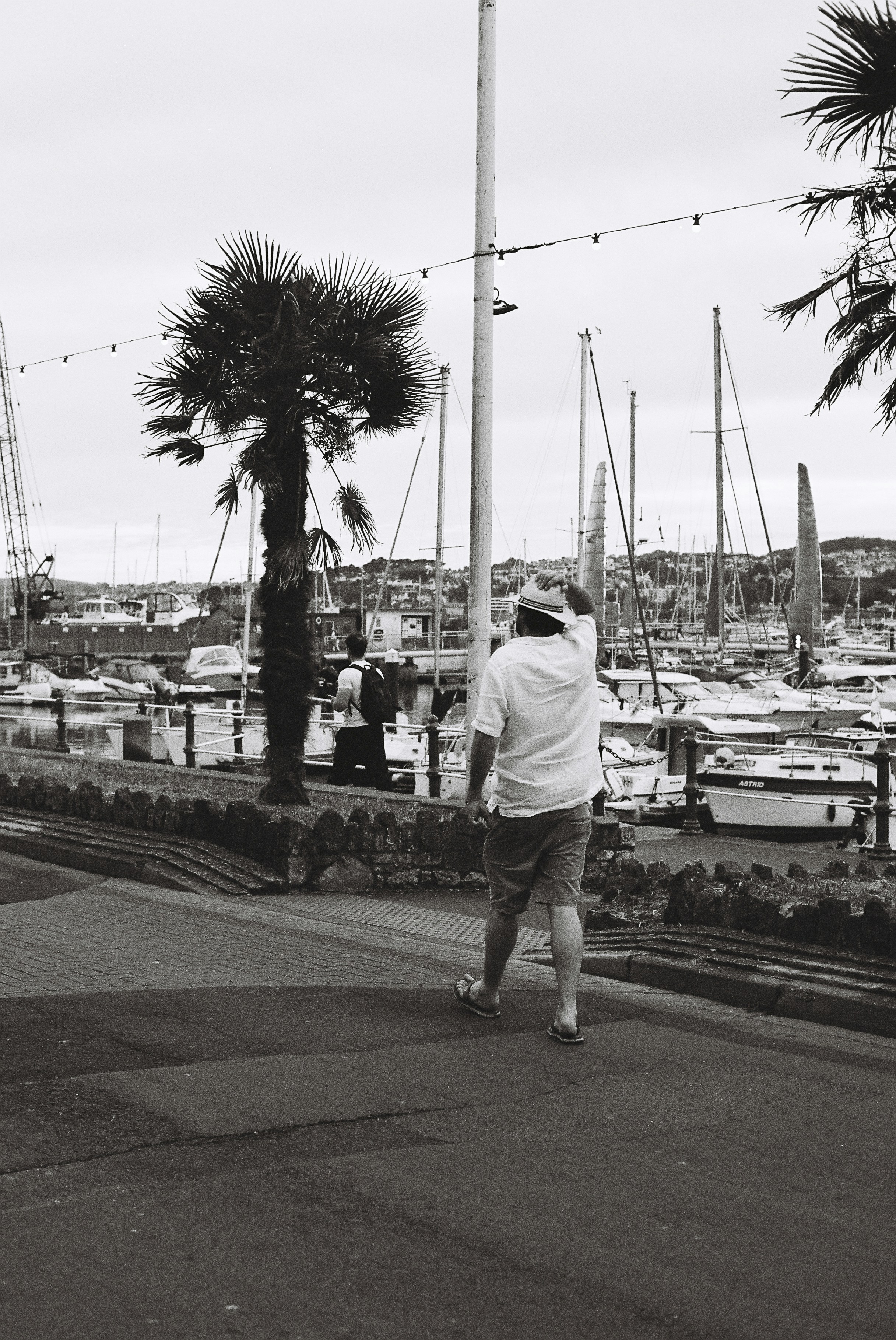 Un hombre pasando junto a barcos y una palmera.