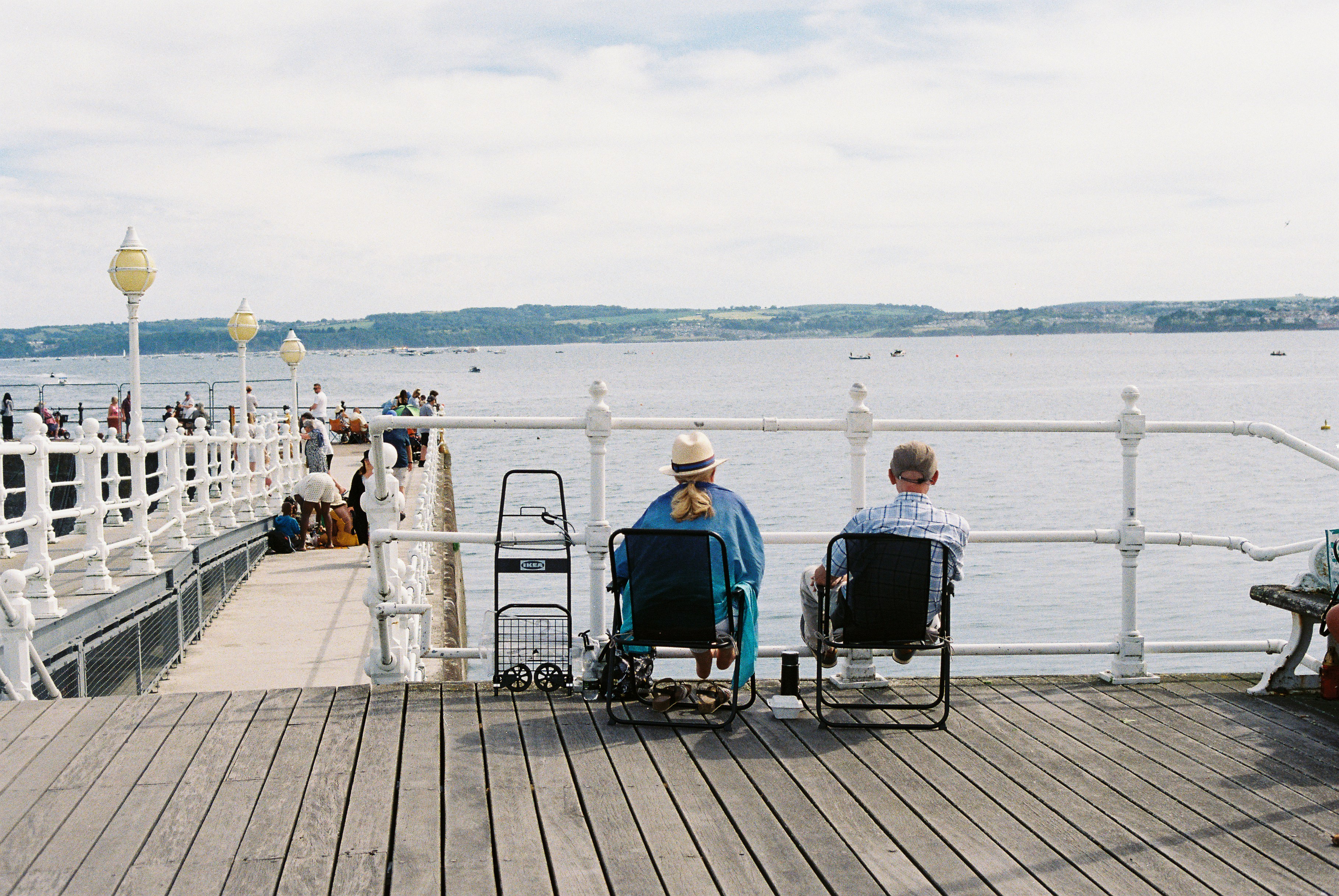 Dos personas sentadas en un muelle, mirando el océano.