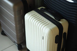 Three hard-shell suitcases in white, grey, and dark colors.