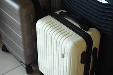Three hard-shell suitcases in white, grey, and dark colors.