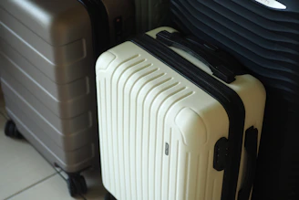 Three hard-shell suitcases in white, grey, and dark colors.