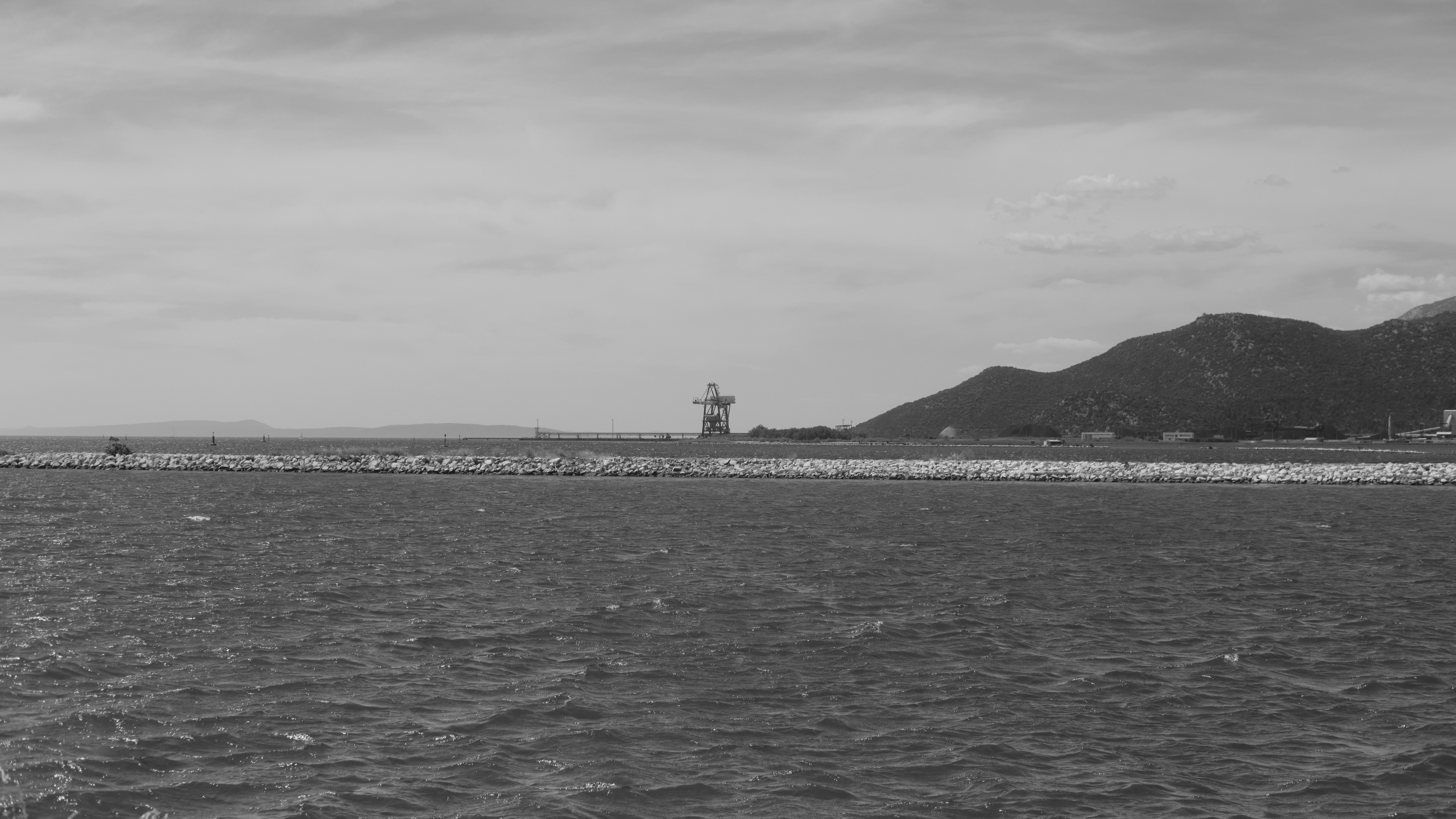 Black and white seascape with a distant lighthouse and mountains.