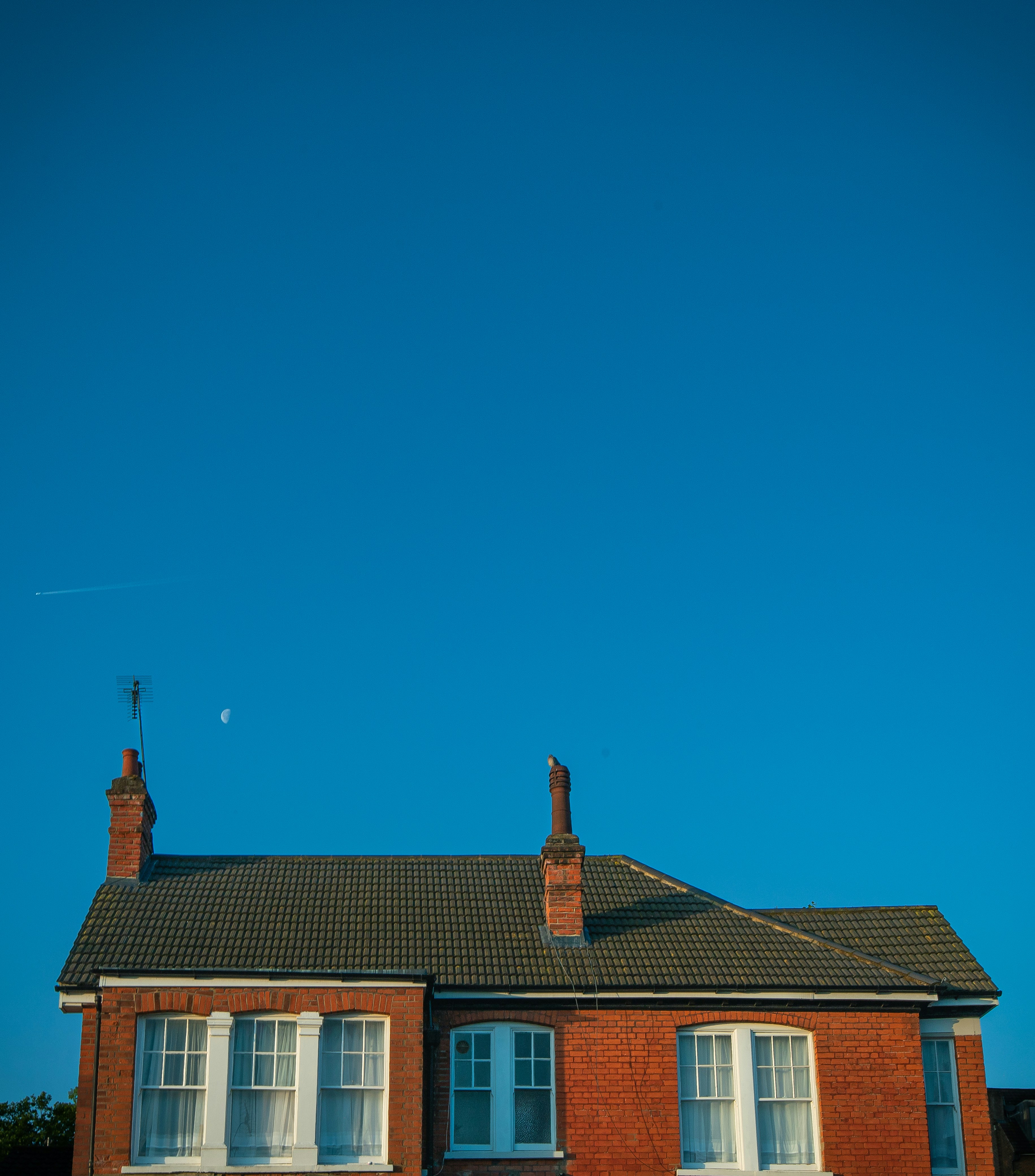 Red brick house with chimneys against a clear blue sky.