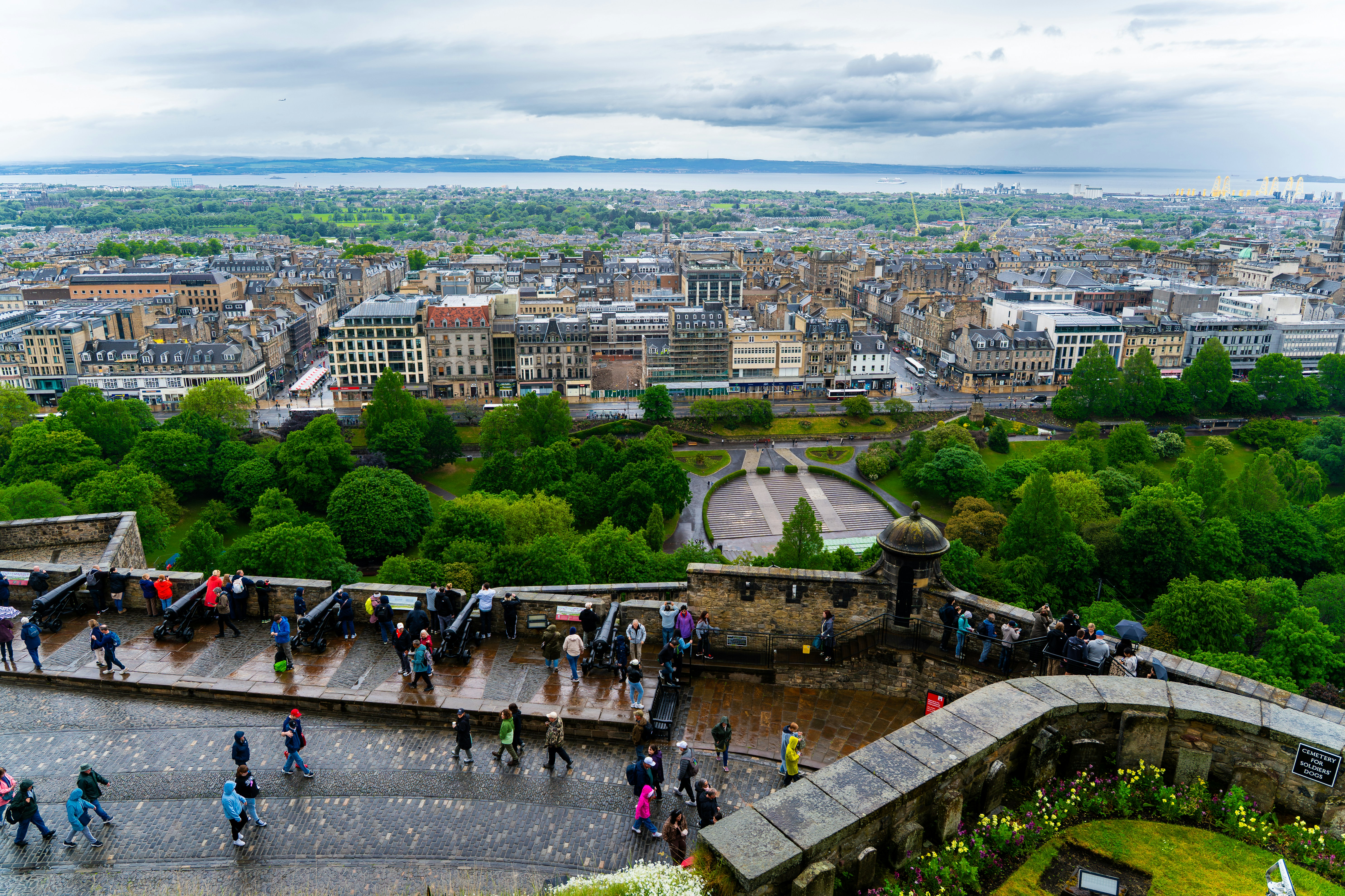 Panorama urbano desde una muralla fortificada con gente y cañones.