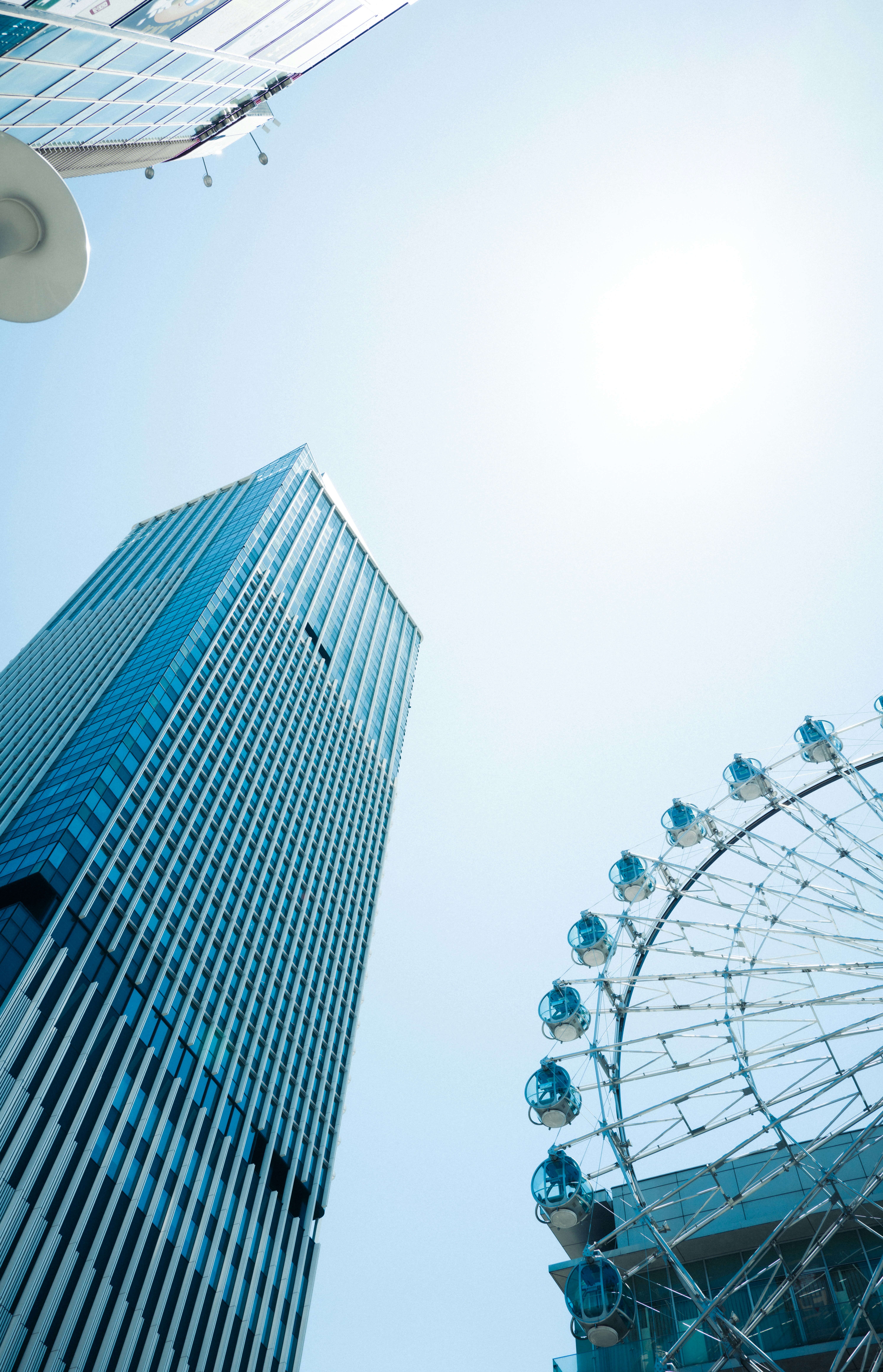 Modern skyscraper and ferris wheel against a bright blue sky.