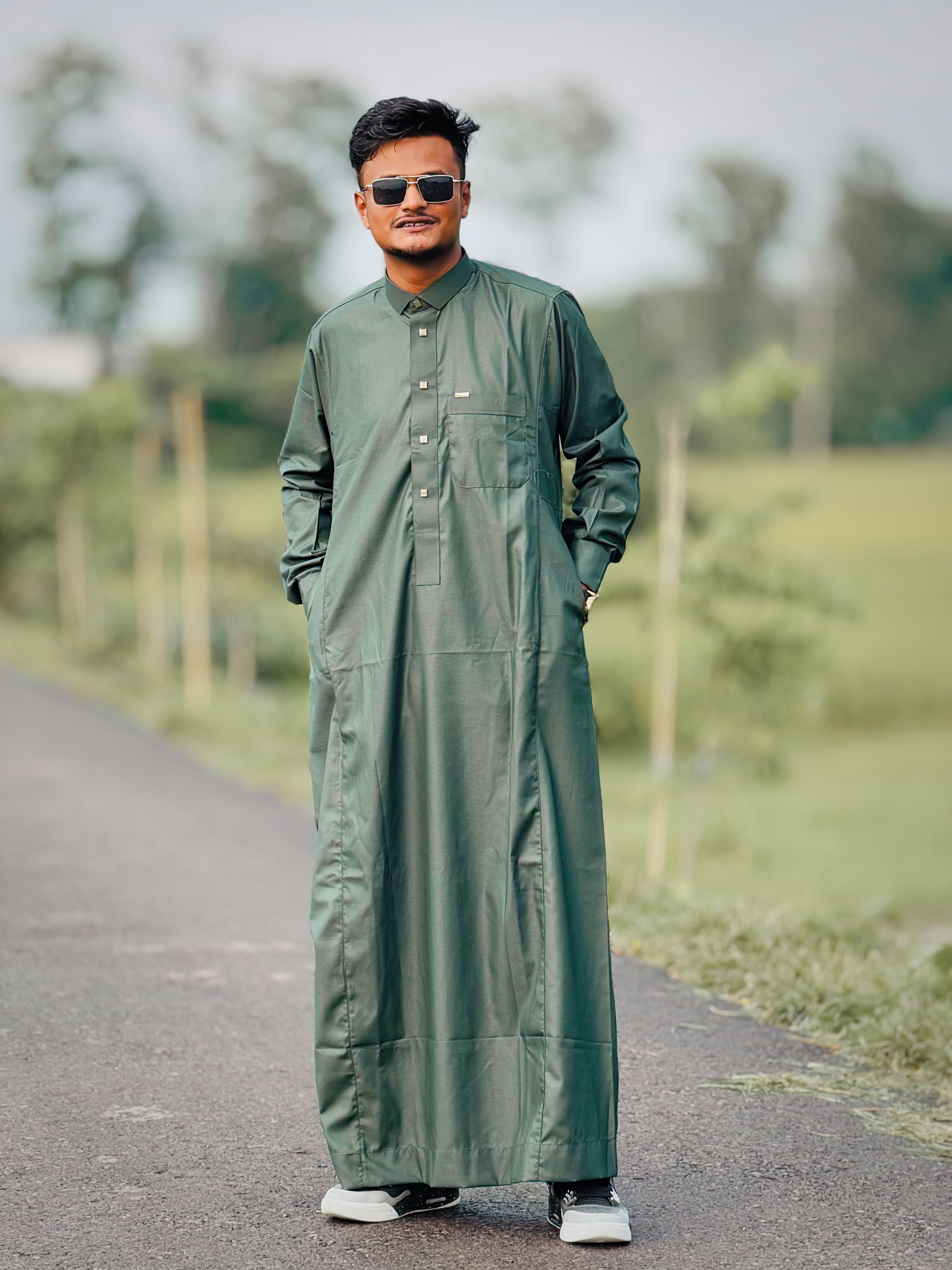 Pria berbaju hijau dan kacamata hitam berdiri di jalan.