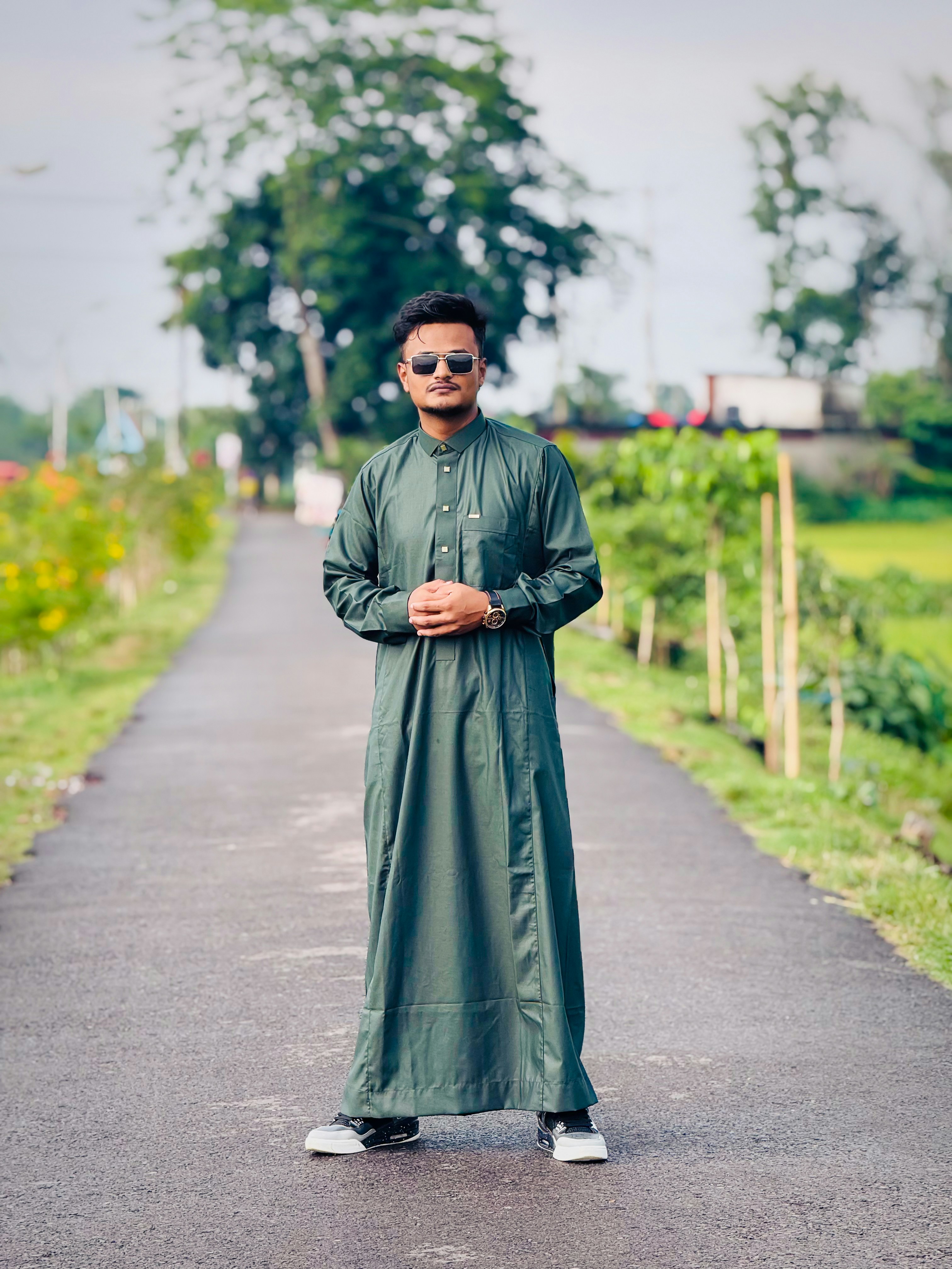 Pria berbaju hijau dan kacamata hitam di jalan luar ruangan.