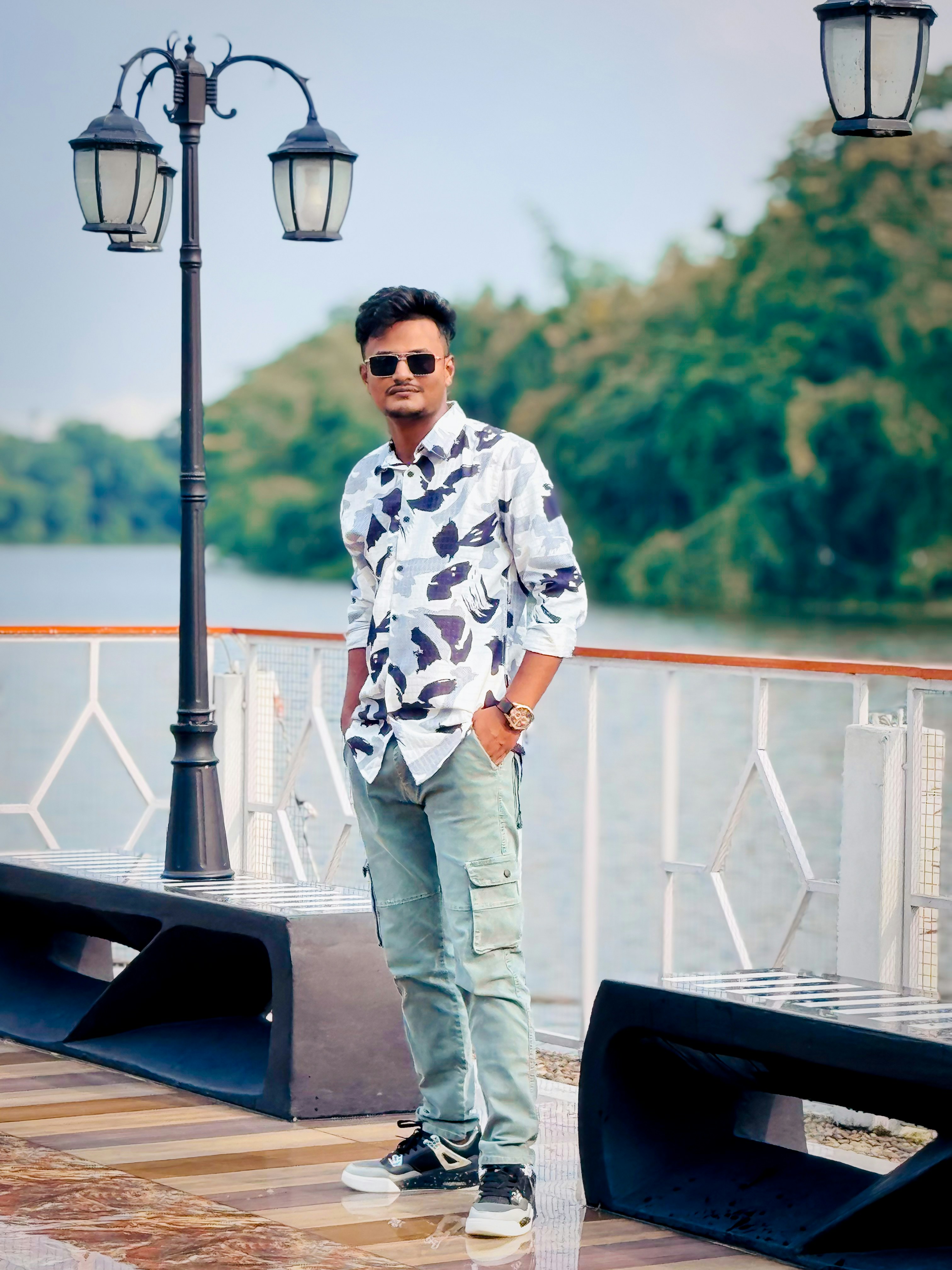 Pria berbaju bermotif berdiri di dekat tiang lampu di dekat air.