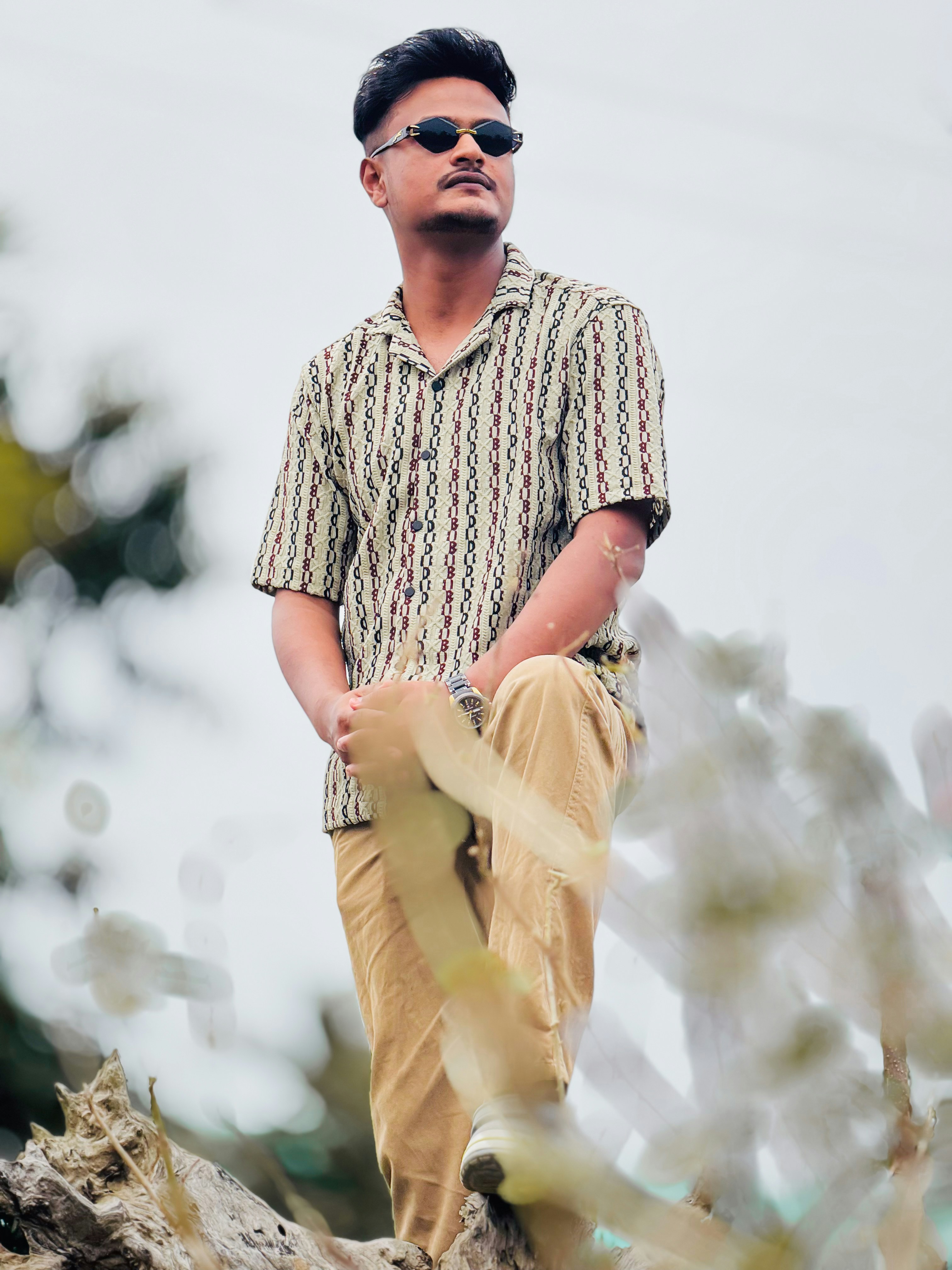 Pria bergaya dengan kacamata hitam dan kemeja bermotif berdiri di luar.