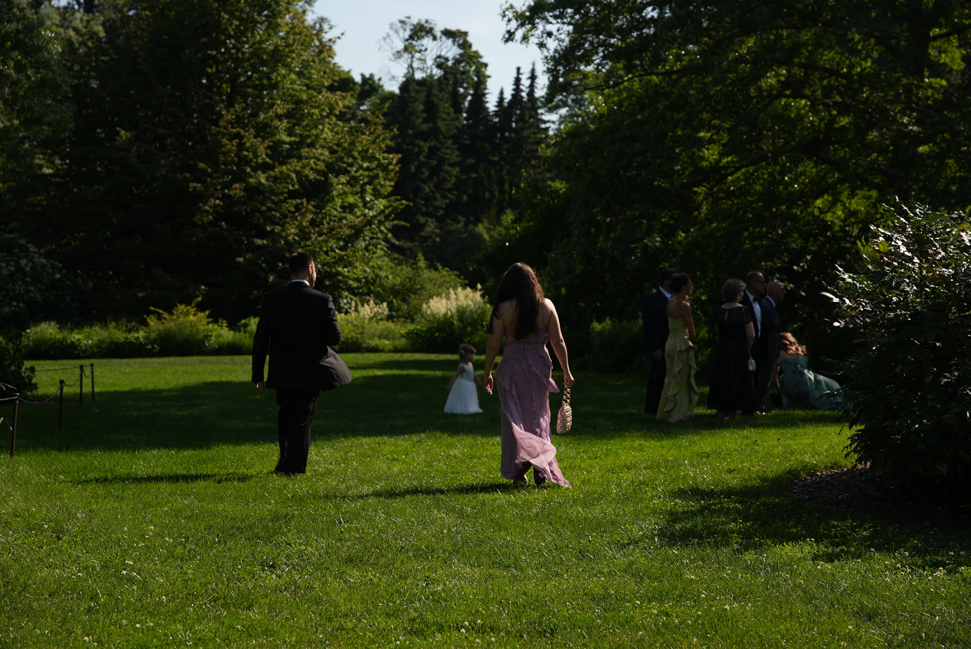 Wedding guests in formal attire walking across a sunny green lawn