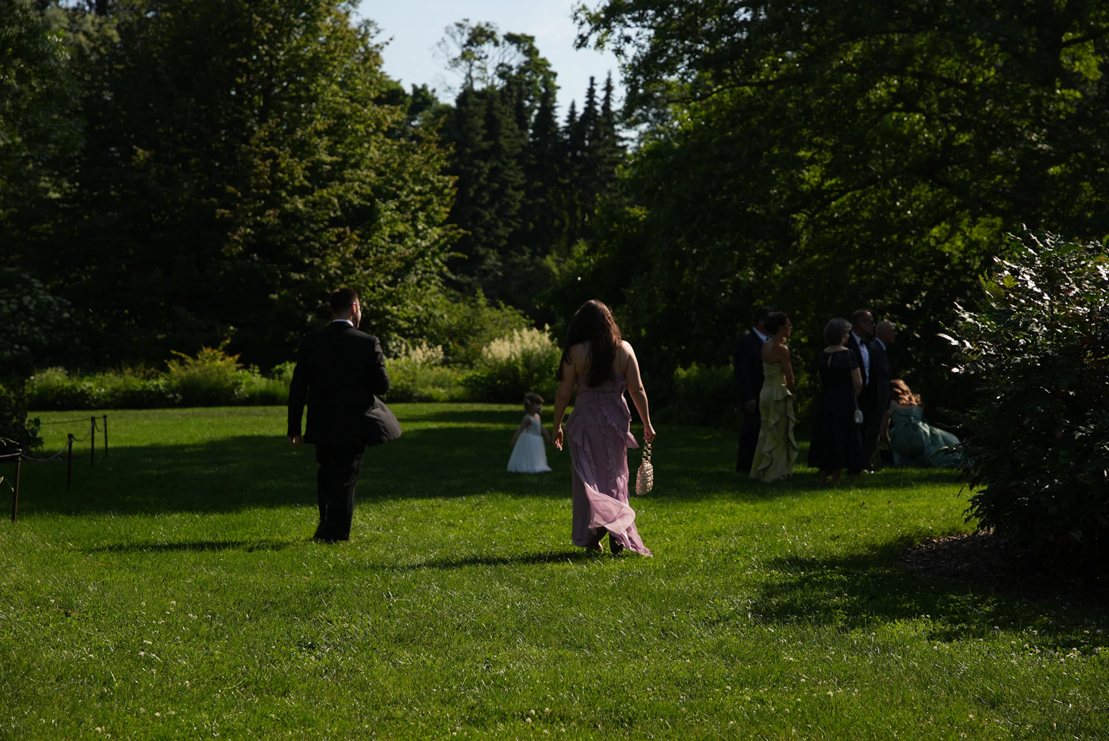 Wedding guests in formal attire walking across a sunny green lawn