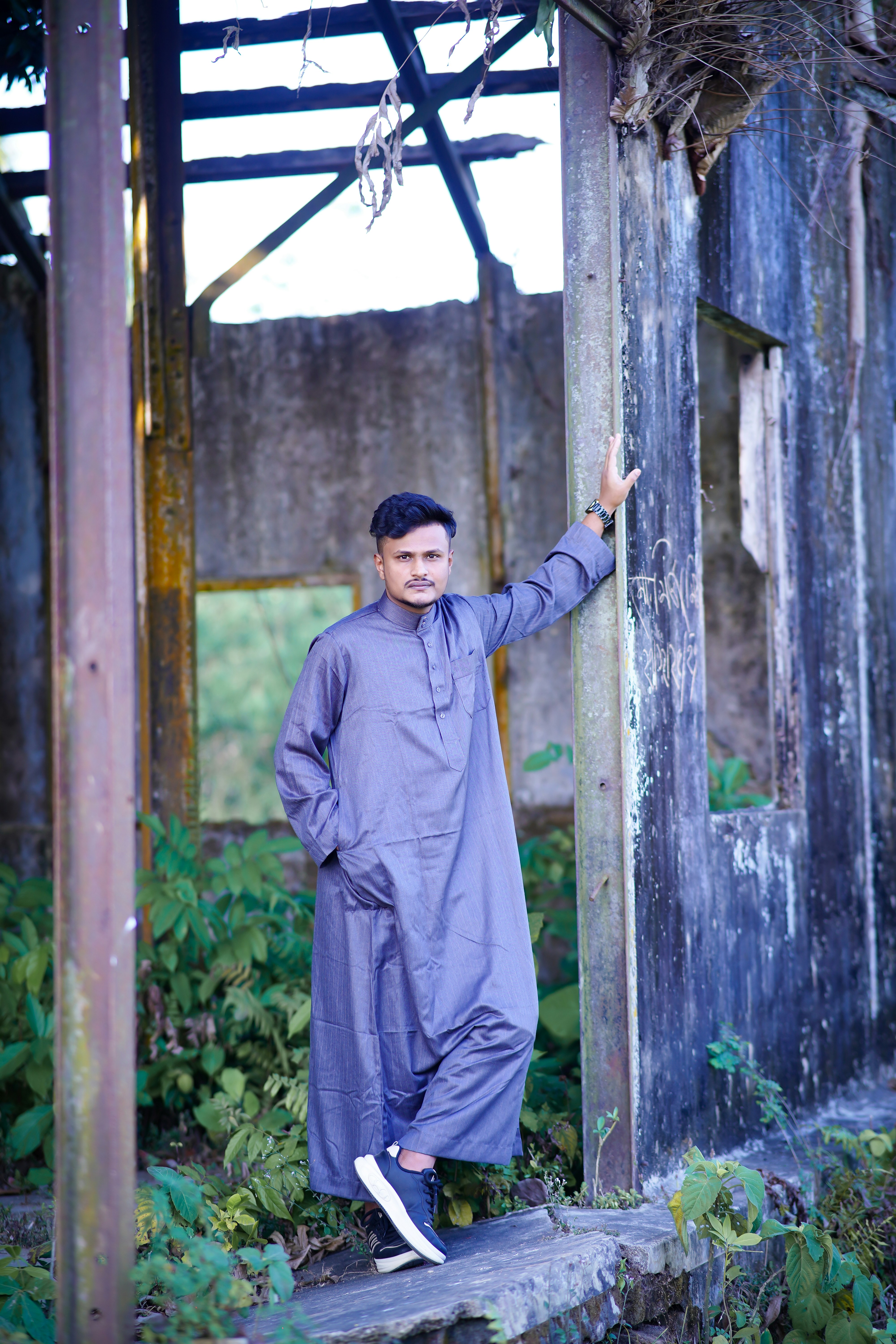 Pria berbaju abu-abu berdiri di dekat struktur kayu lapuk.