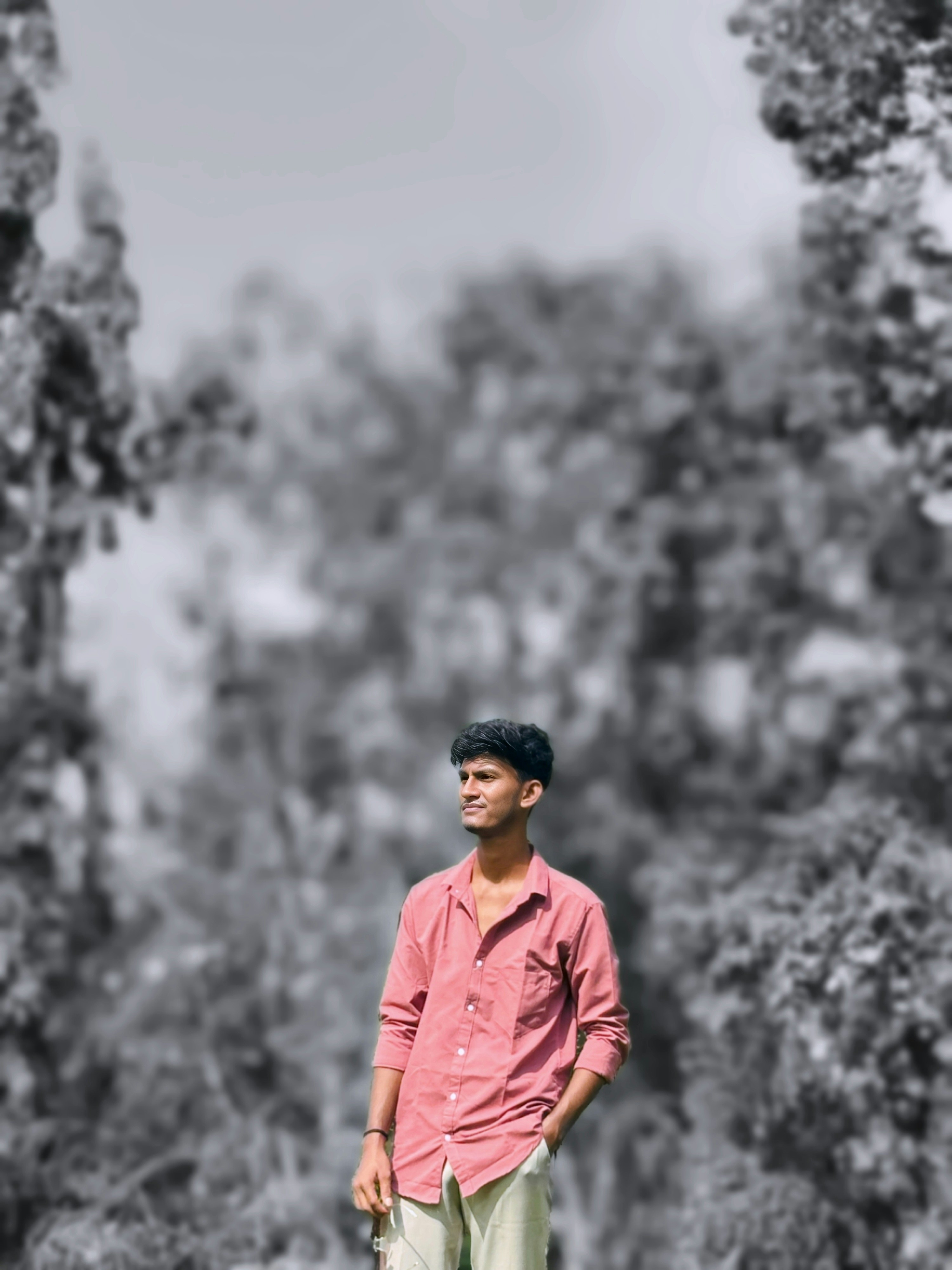 Um jovem de camisa rosa contra árvores borradas.