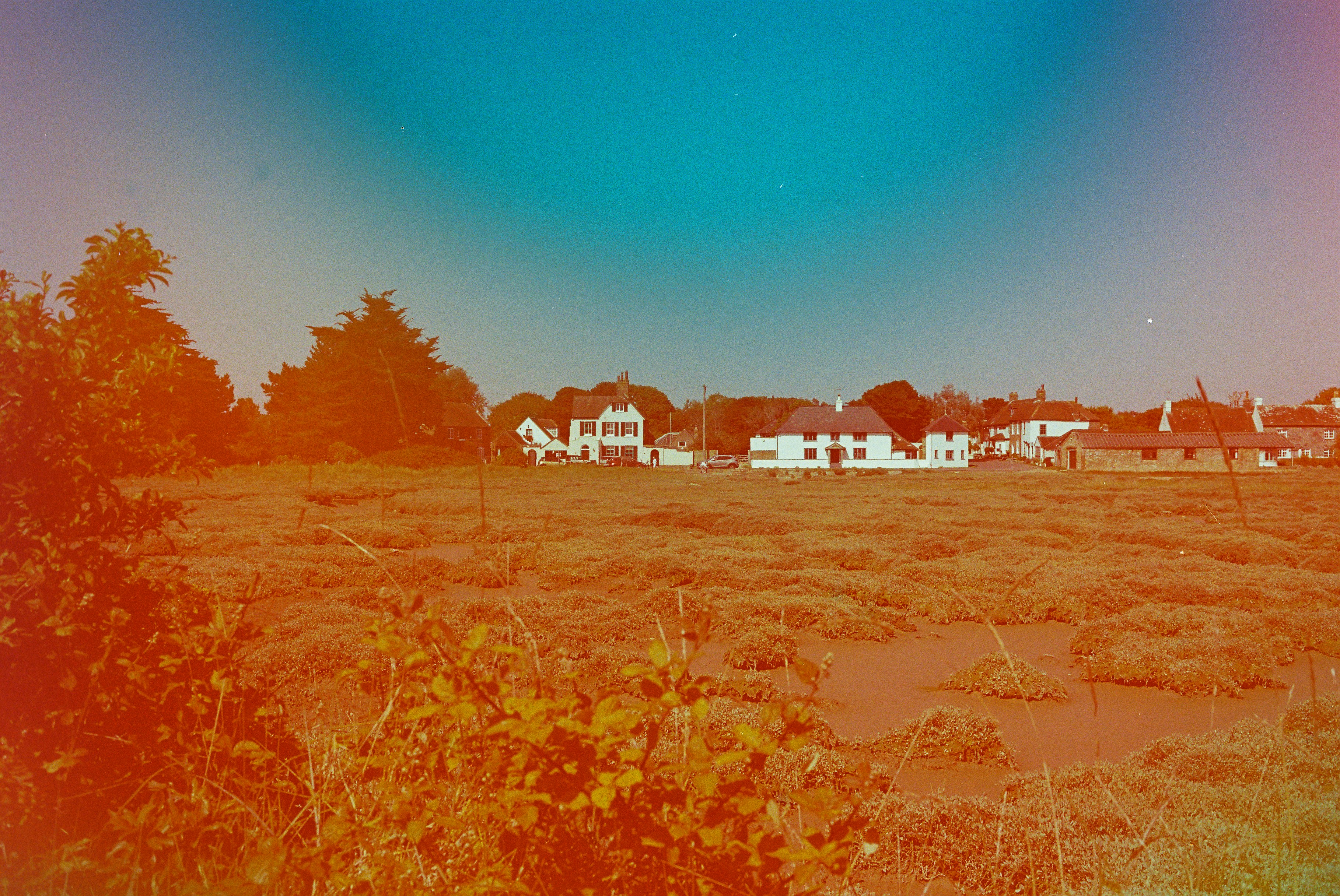 Campo de feno seco com casas distantes sob um céu colorido.