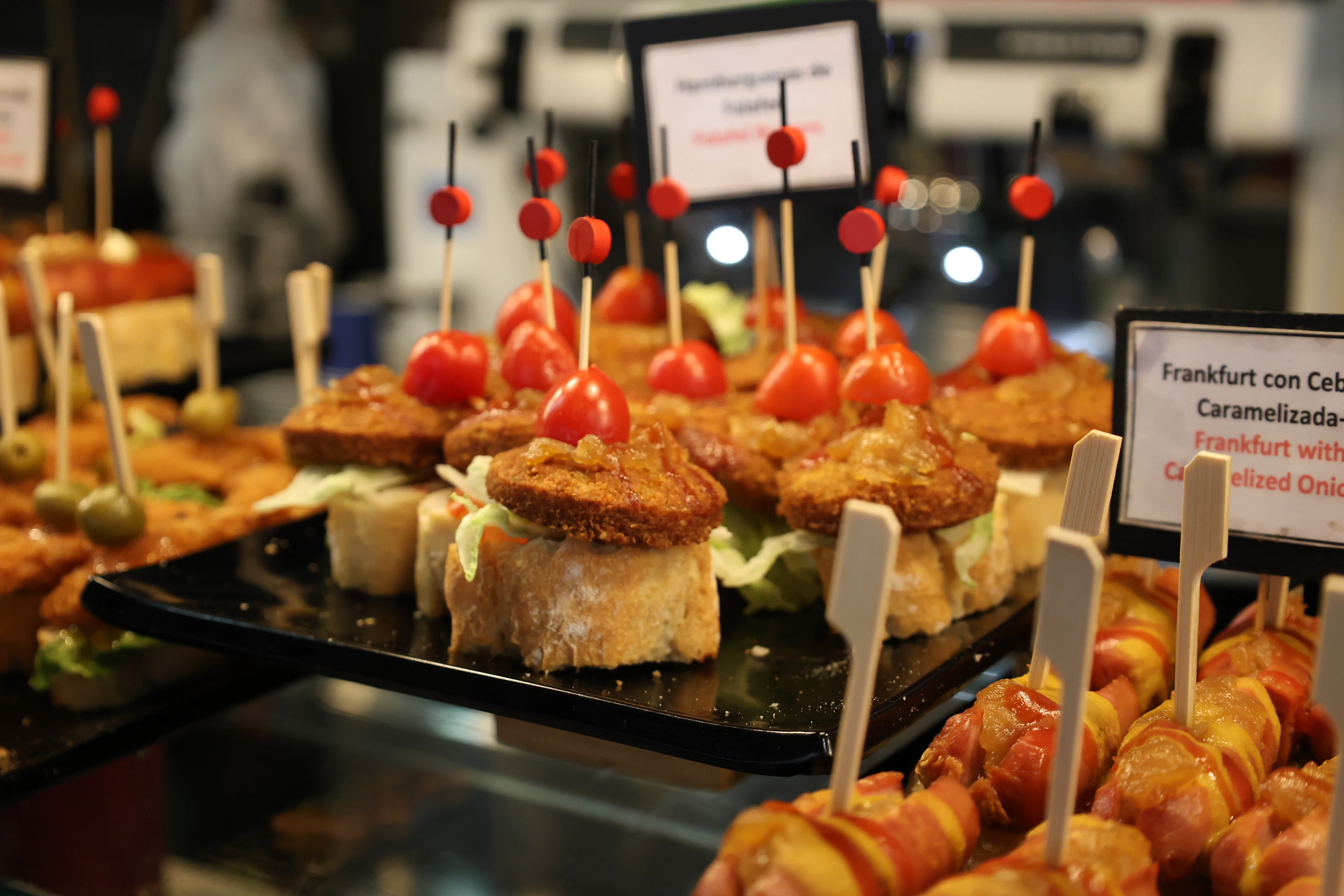 A tapas bar counter crowded with skewered pintxos topped with cherry tomatoes and croquettes