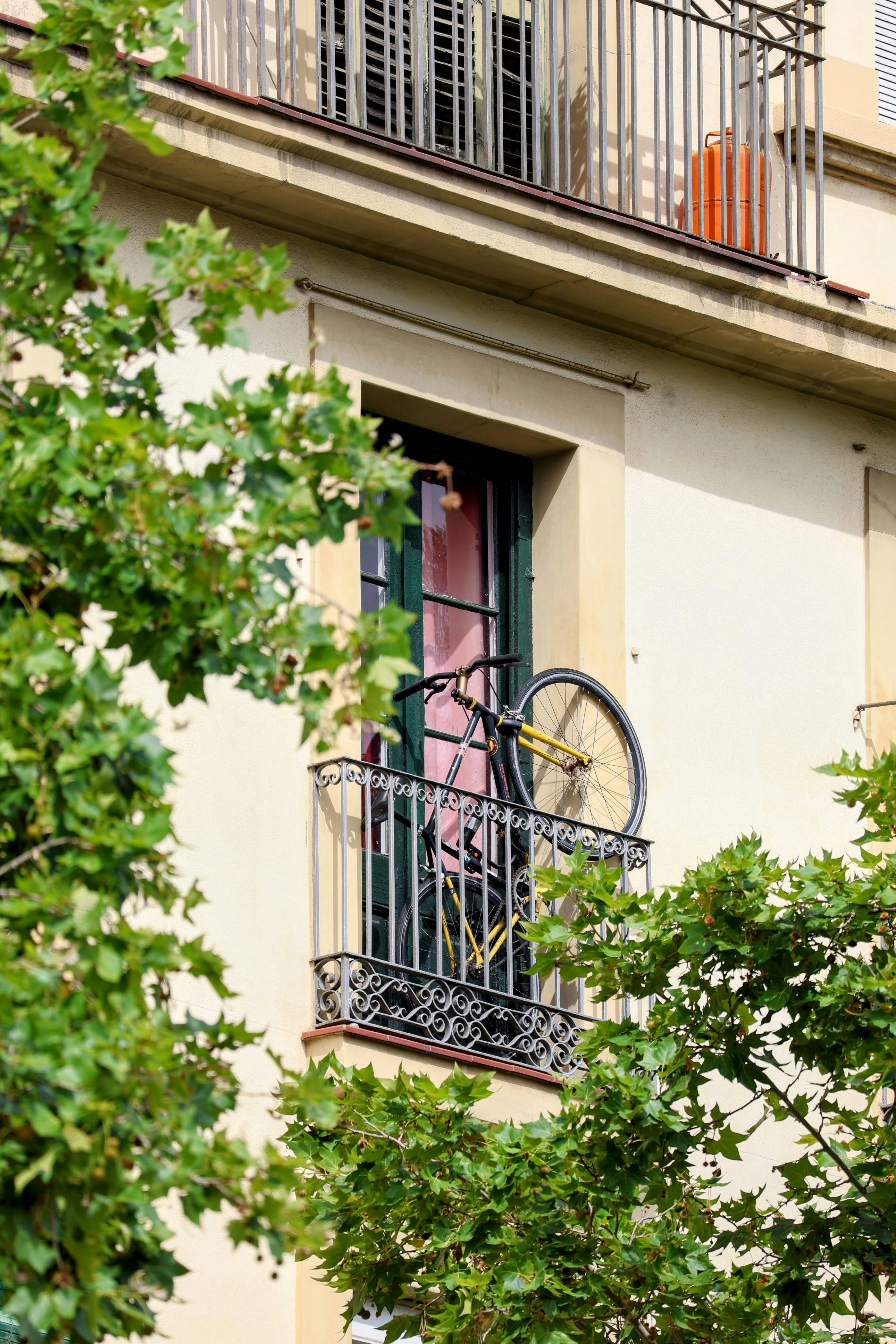 A bicycle hangs on a balcony railing amidst green leaves.