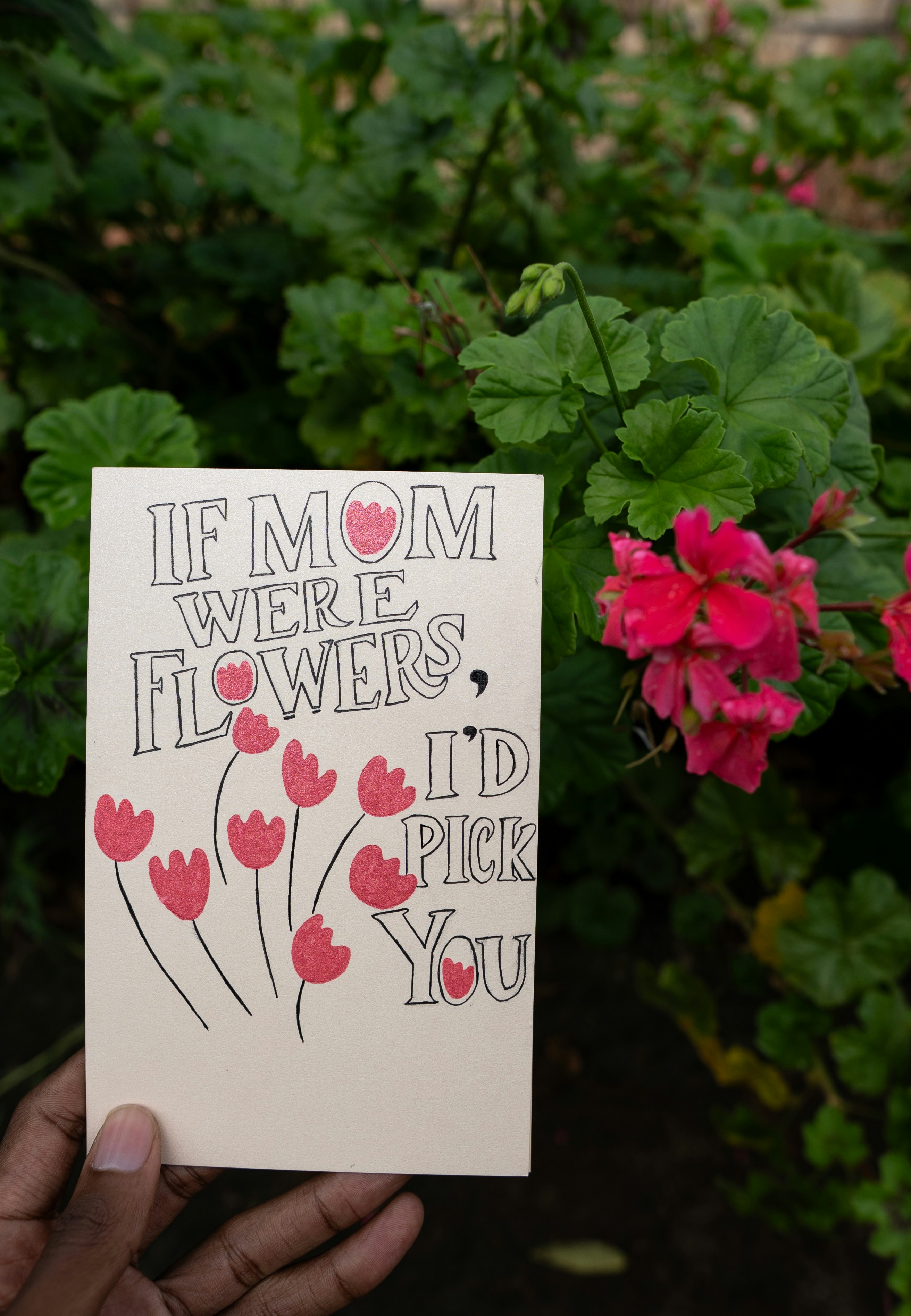 Segurando um cartão de Dia das Mães com desenhos de flores vermelhas.