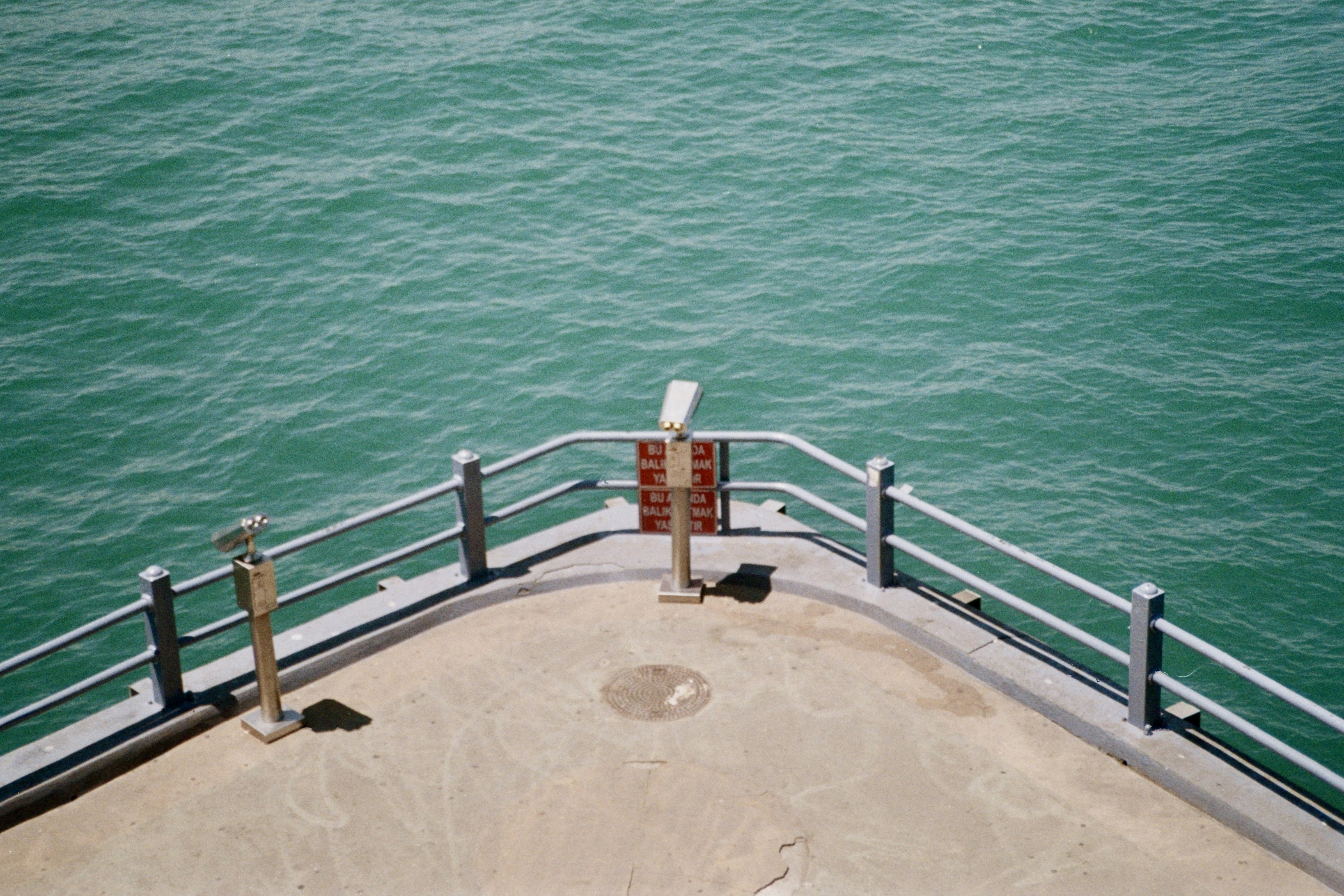A pier overlooking turquoise ocean water with coin-operated binoculars.