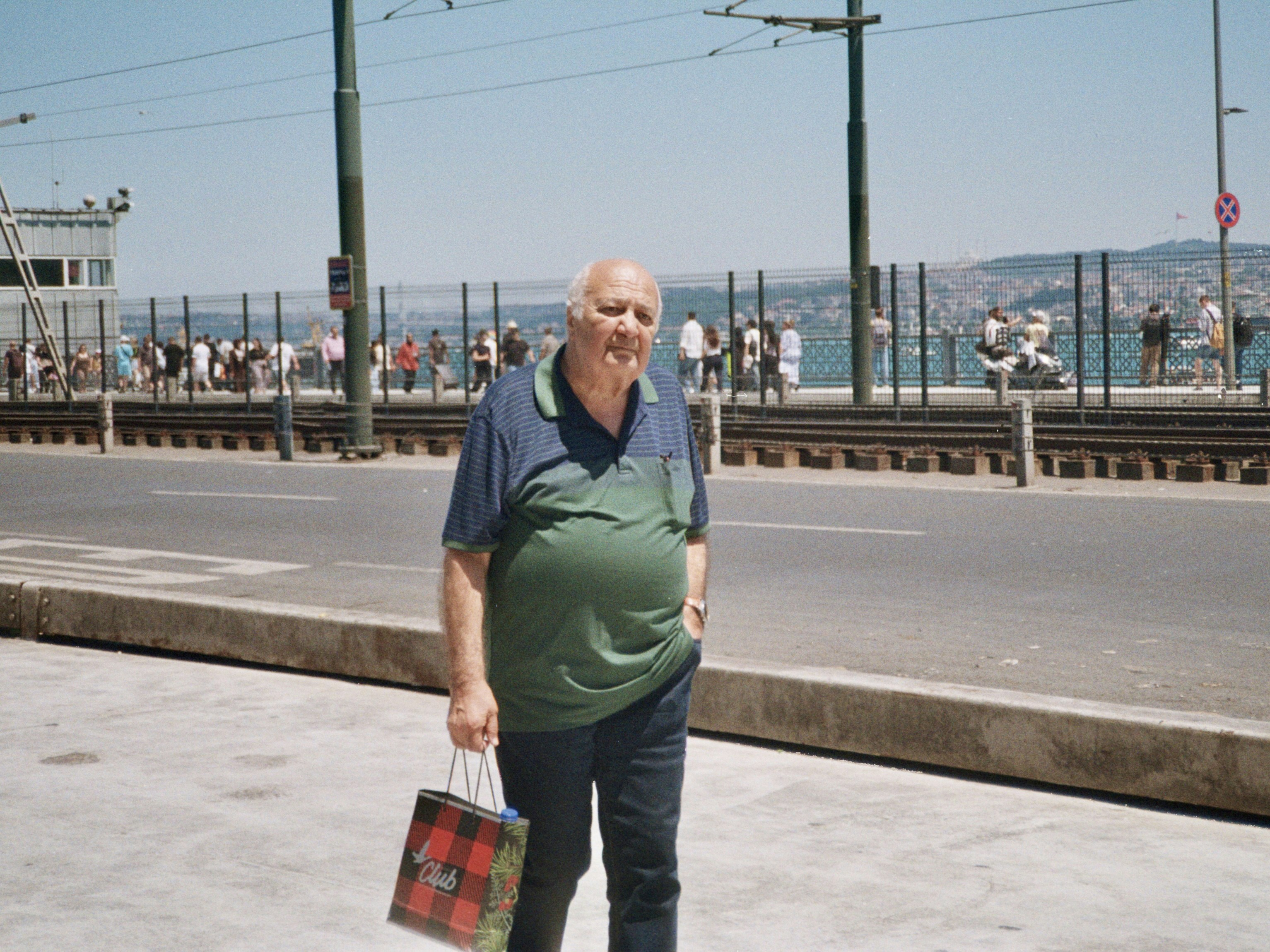 Man walking on a sunny street with a shopping bag.