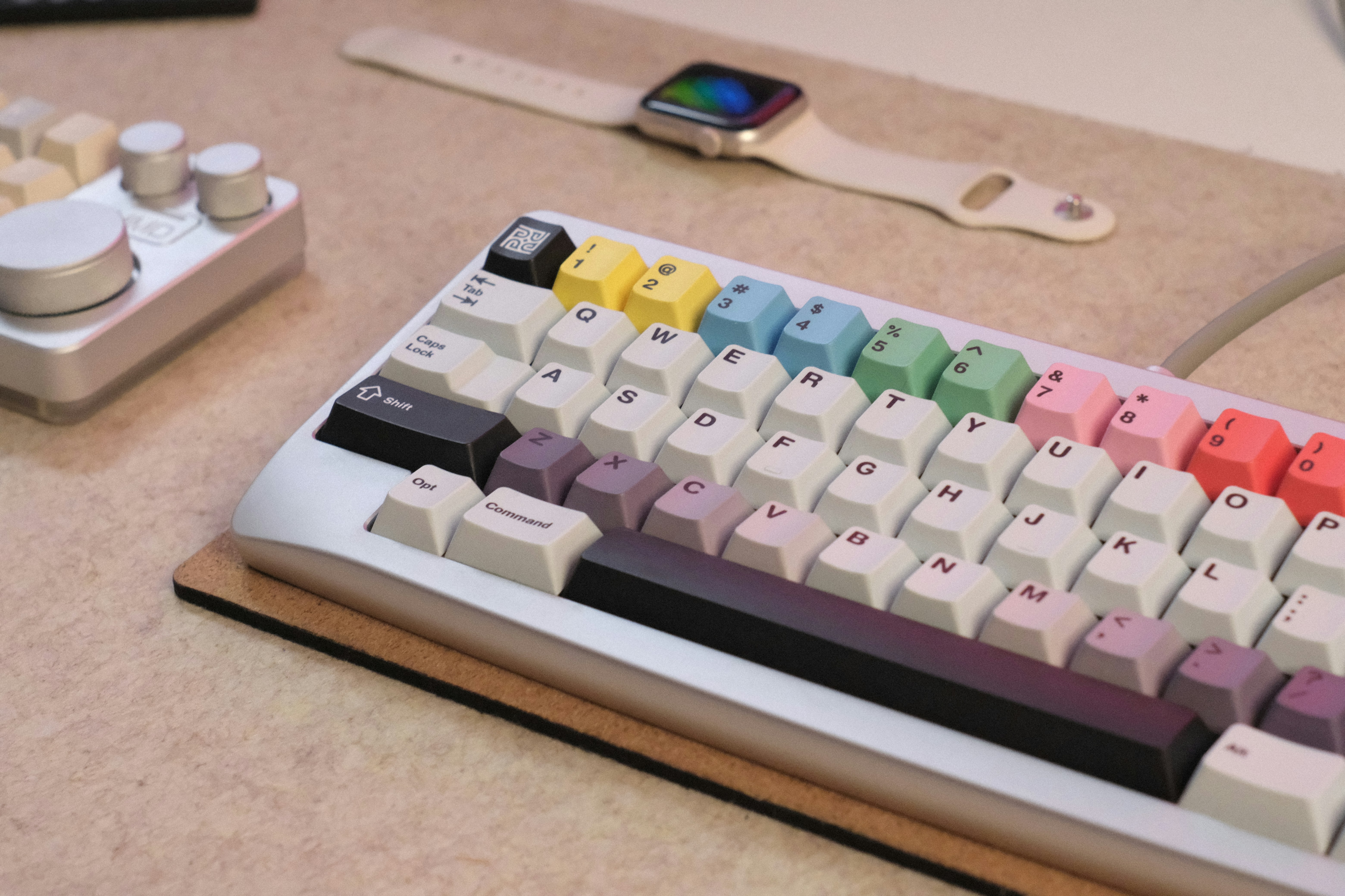 Colorful mechanical keyboard, smartwatch, and control knob on a desk.