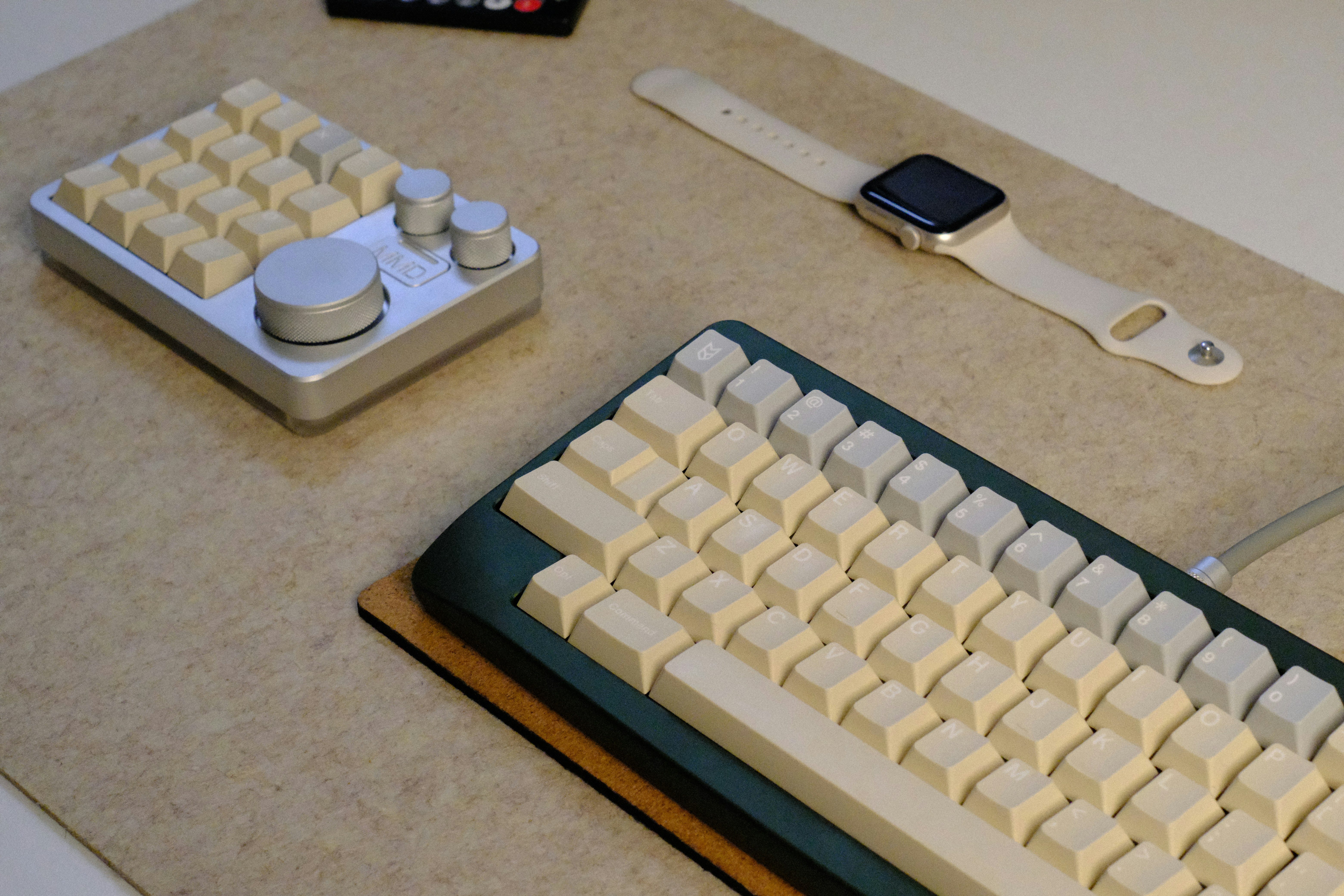 A mechanical keyboard, control pad, and smartwatch on a desk.