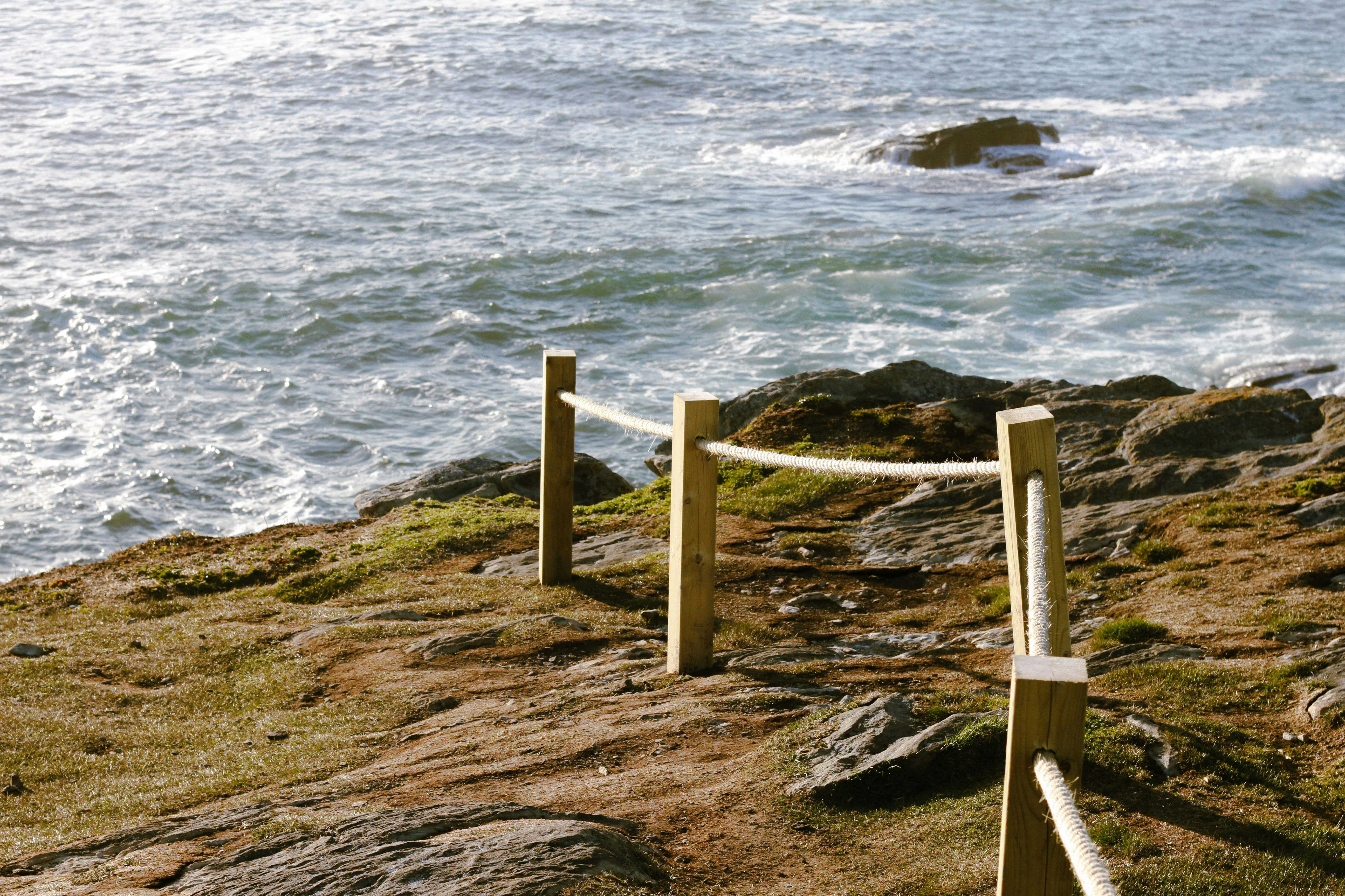 A rope fence lines a rocky coast beside the ocean.