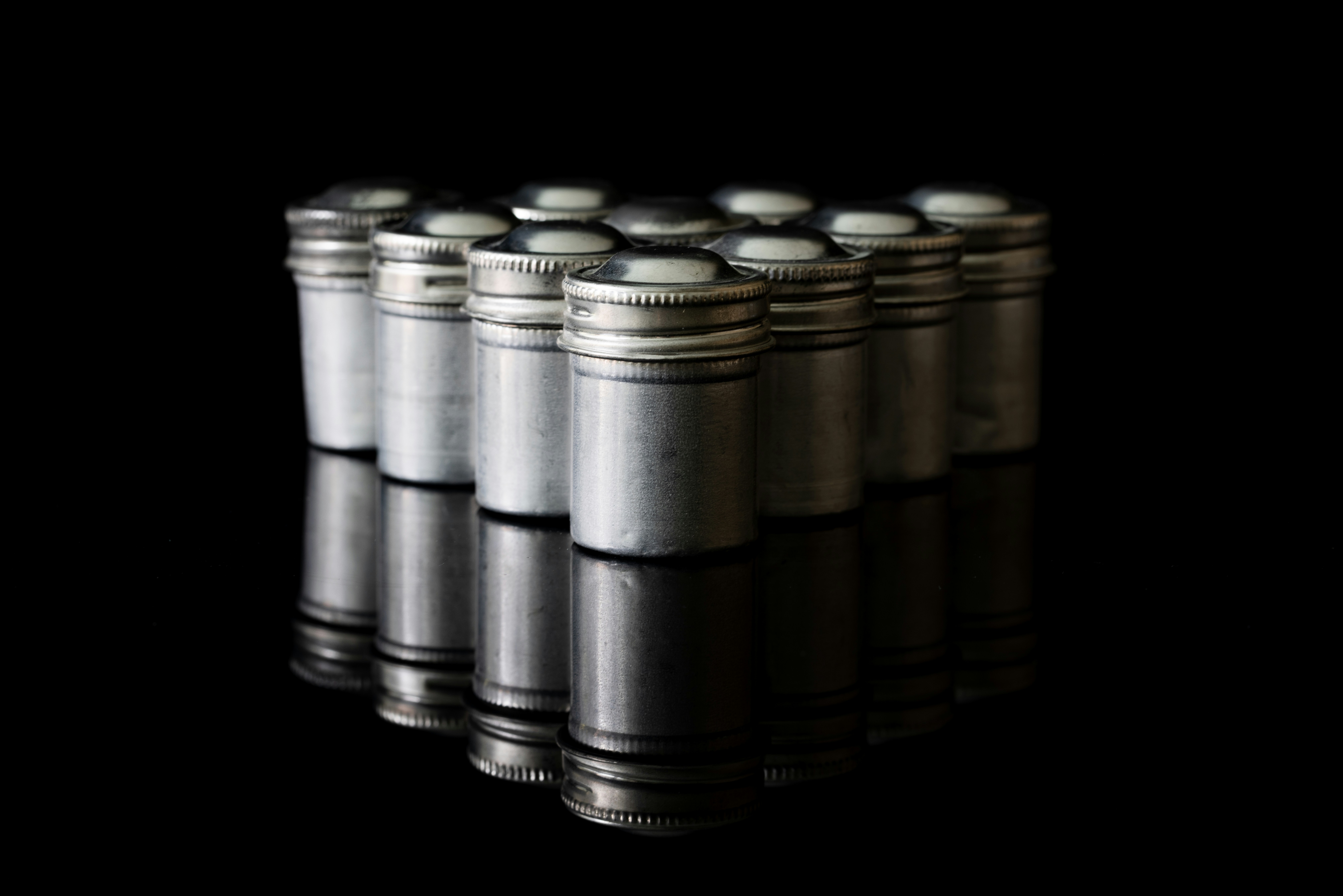 Silver cylindrical containers arranged on a reflective black surface.
