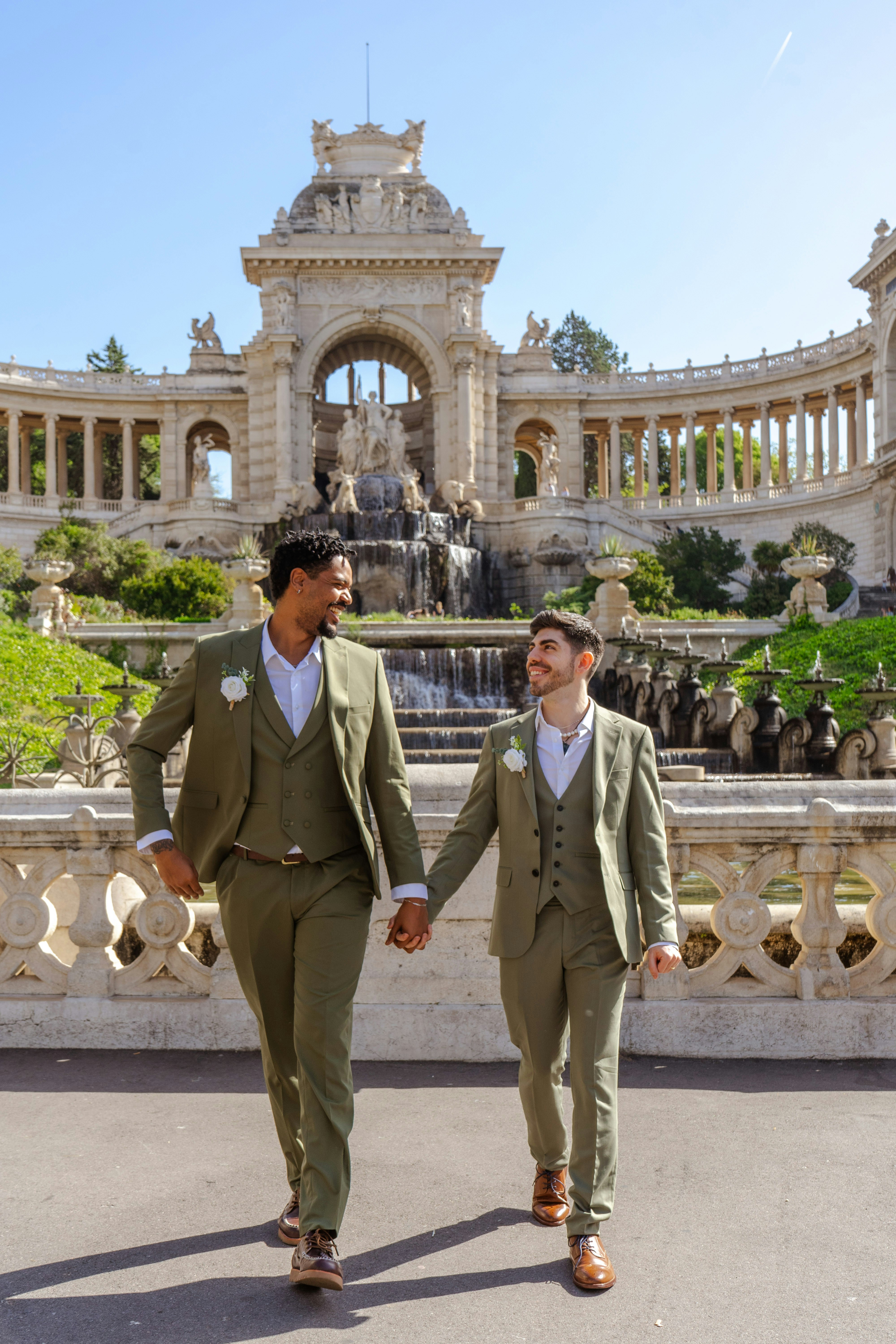 Happy couple in green suits holding hands near ornate building