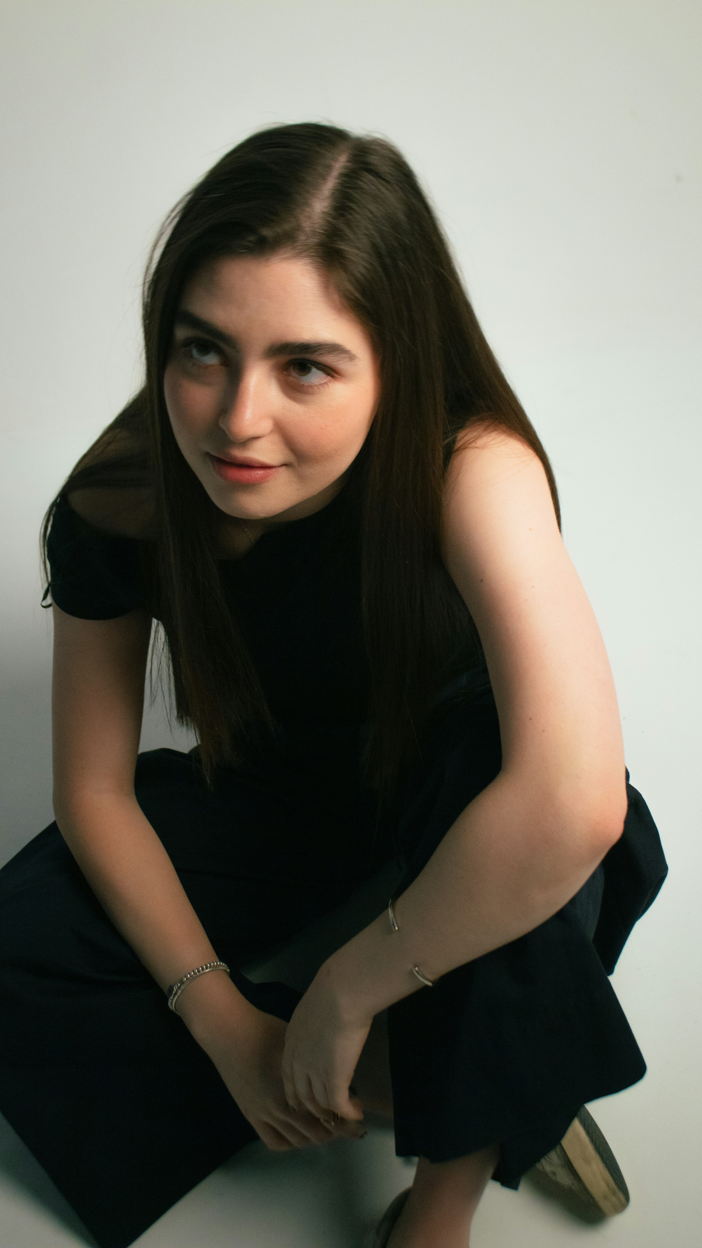 Young woman in black clothing crouching on a white background