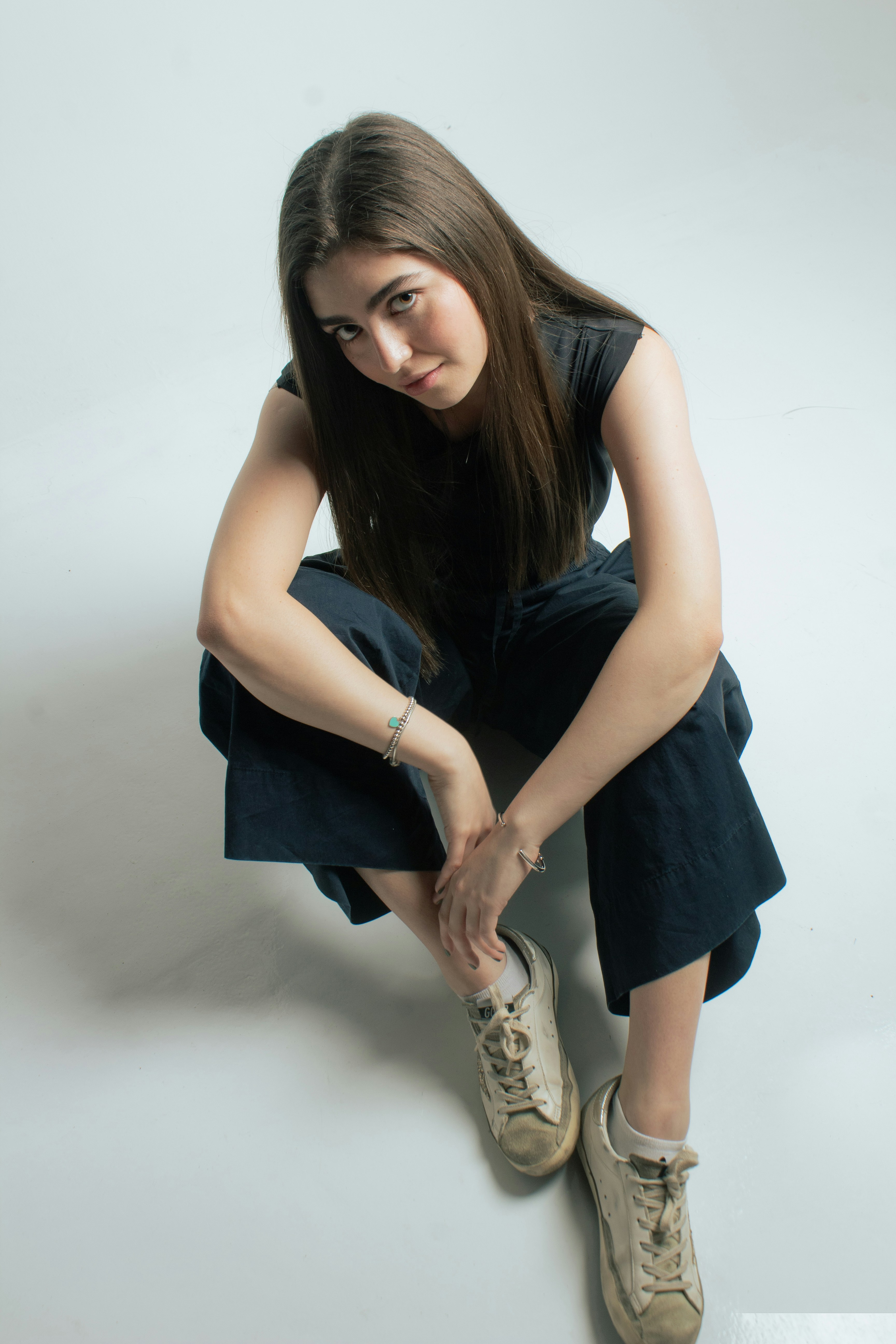 Young woman with dark hair crouching on a white background