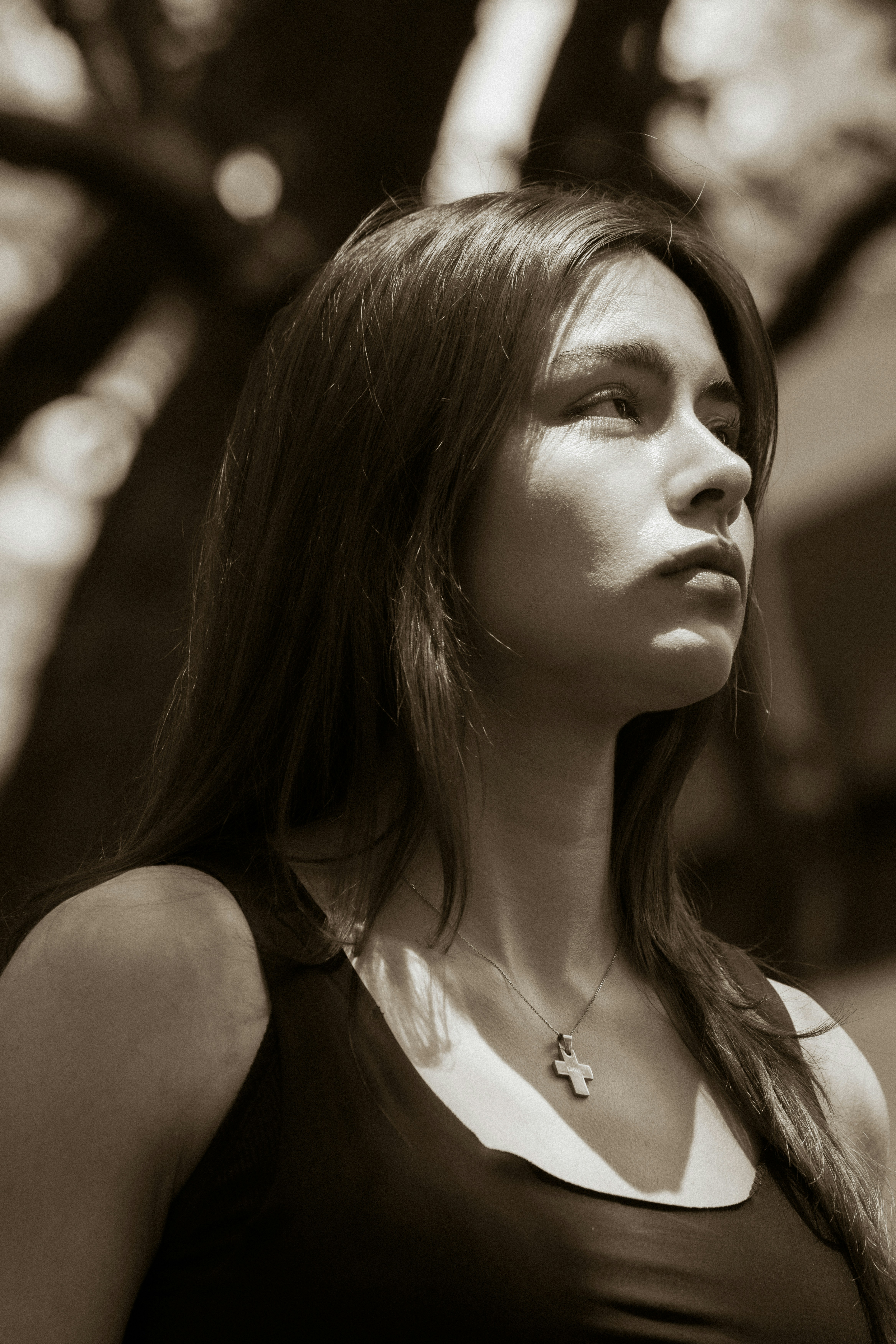 Young woman with cross necklace looking up in sepia