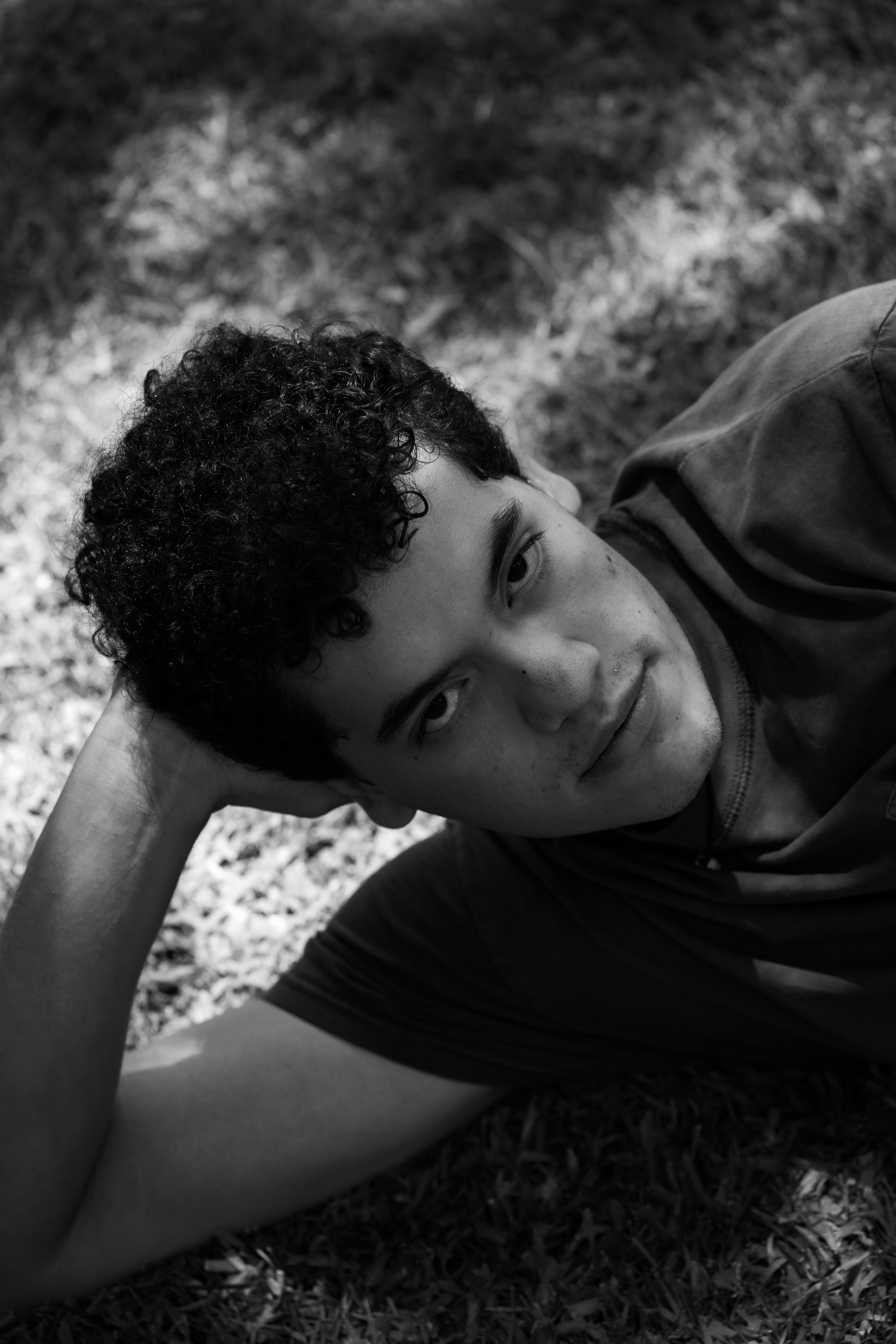 A young man with curly hair lies on grass