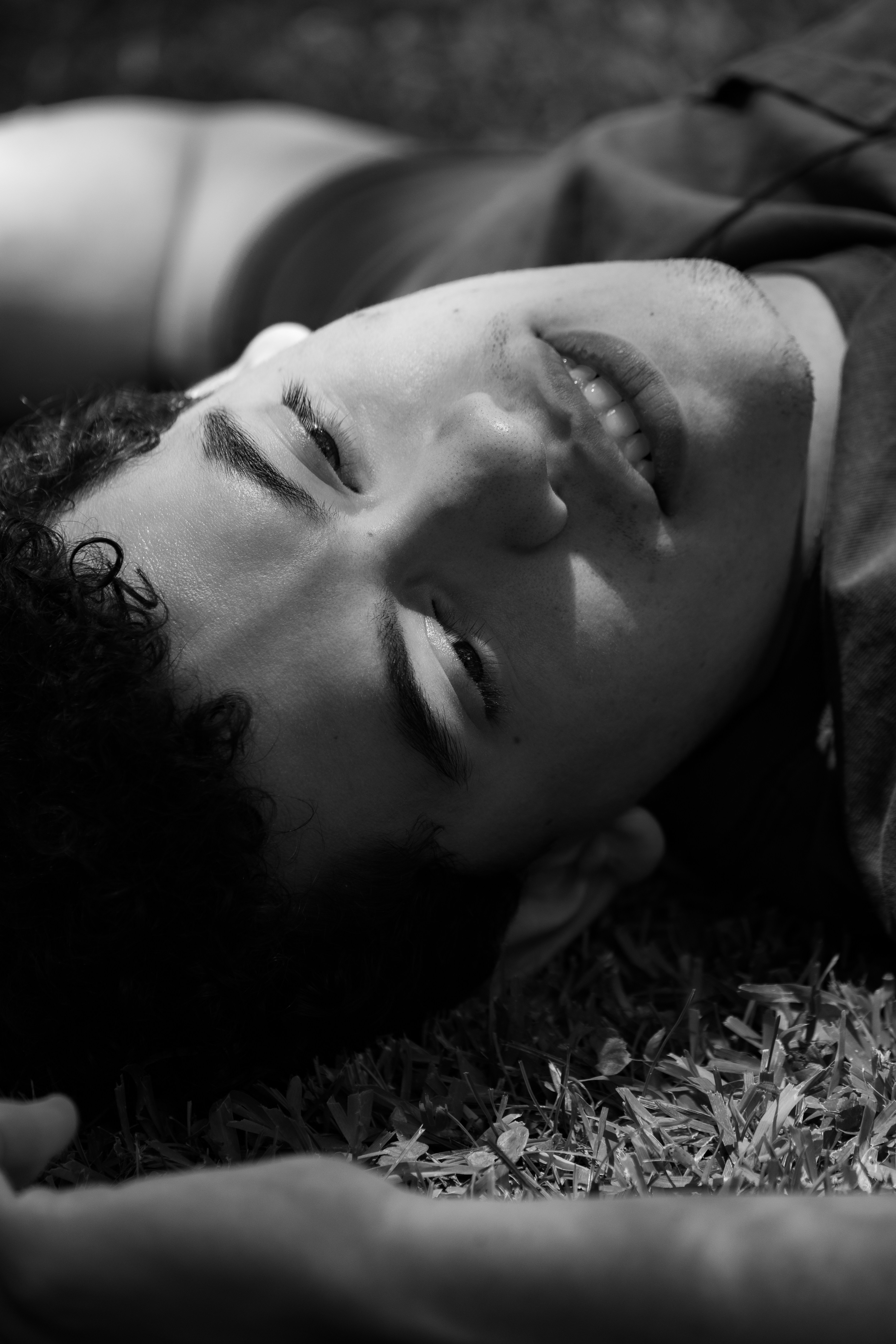 Smiling young person lying on grass, black and white