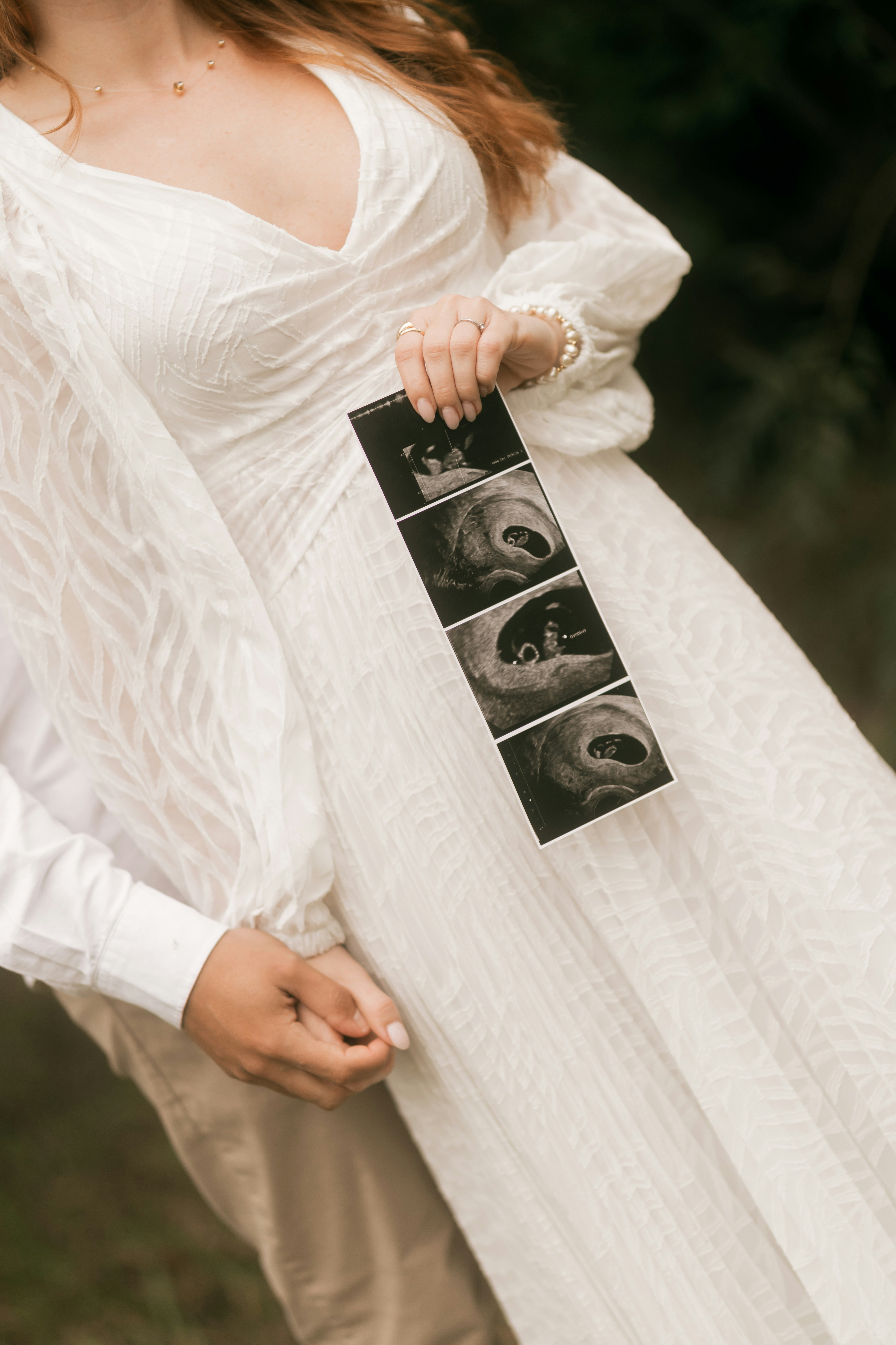 Frau im weißen Kleid hält Ultraschallabzüge mit dem Partner