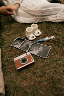 Baby booties, ultrasound photos, pregnancy test, and camera on grass.