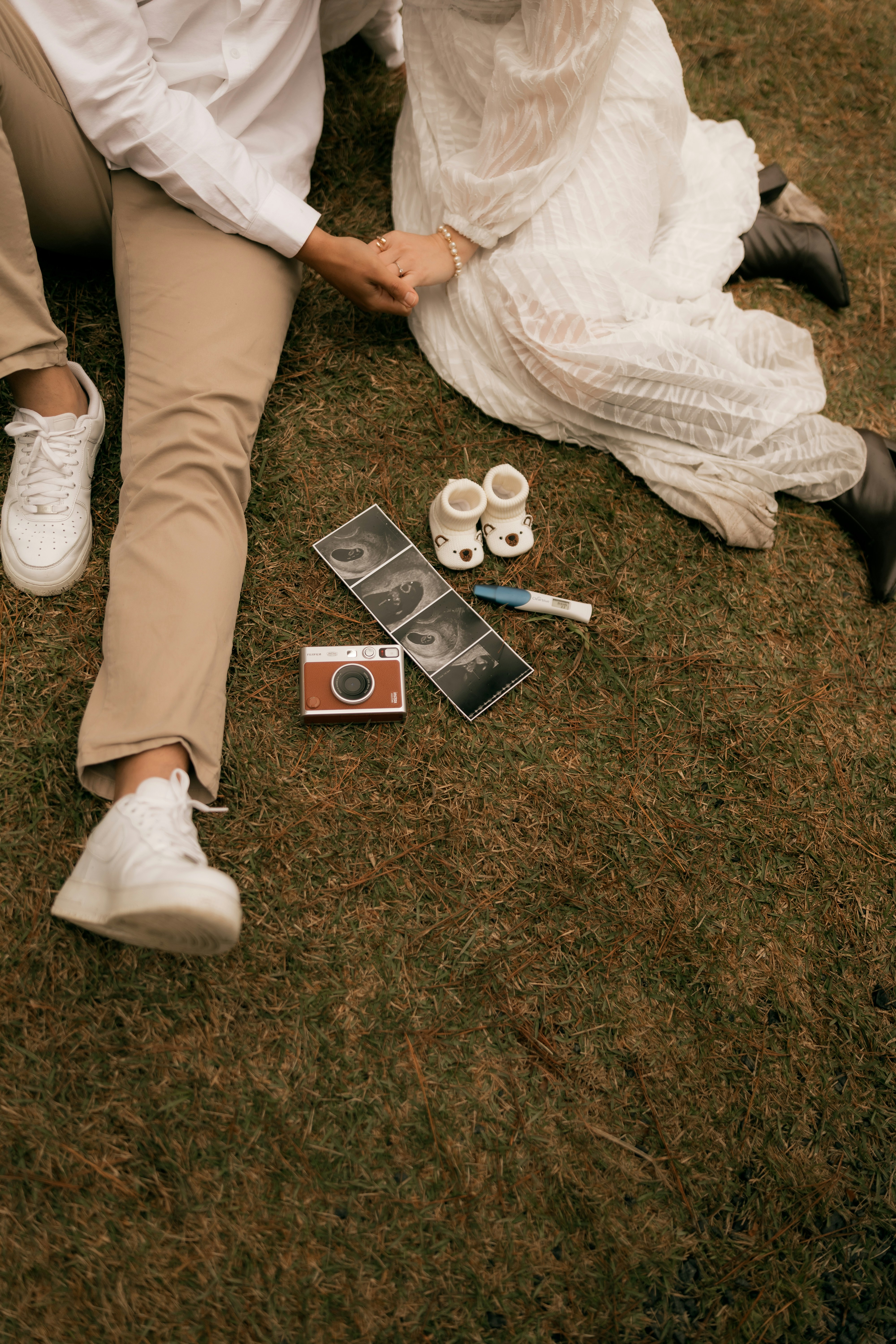 Couple on grass with baby ultrasound, shoes, and camera.
