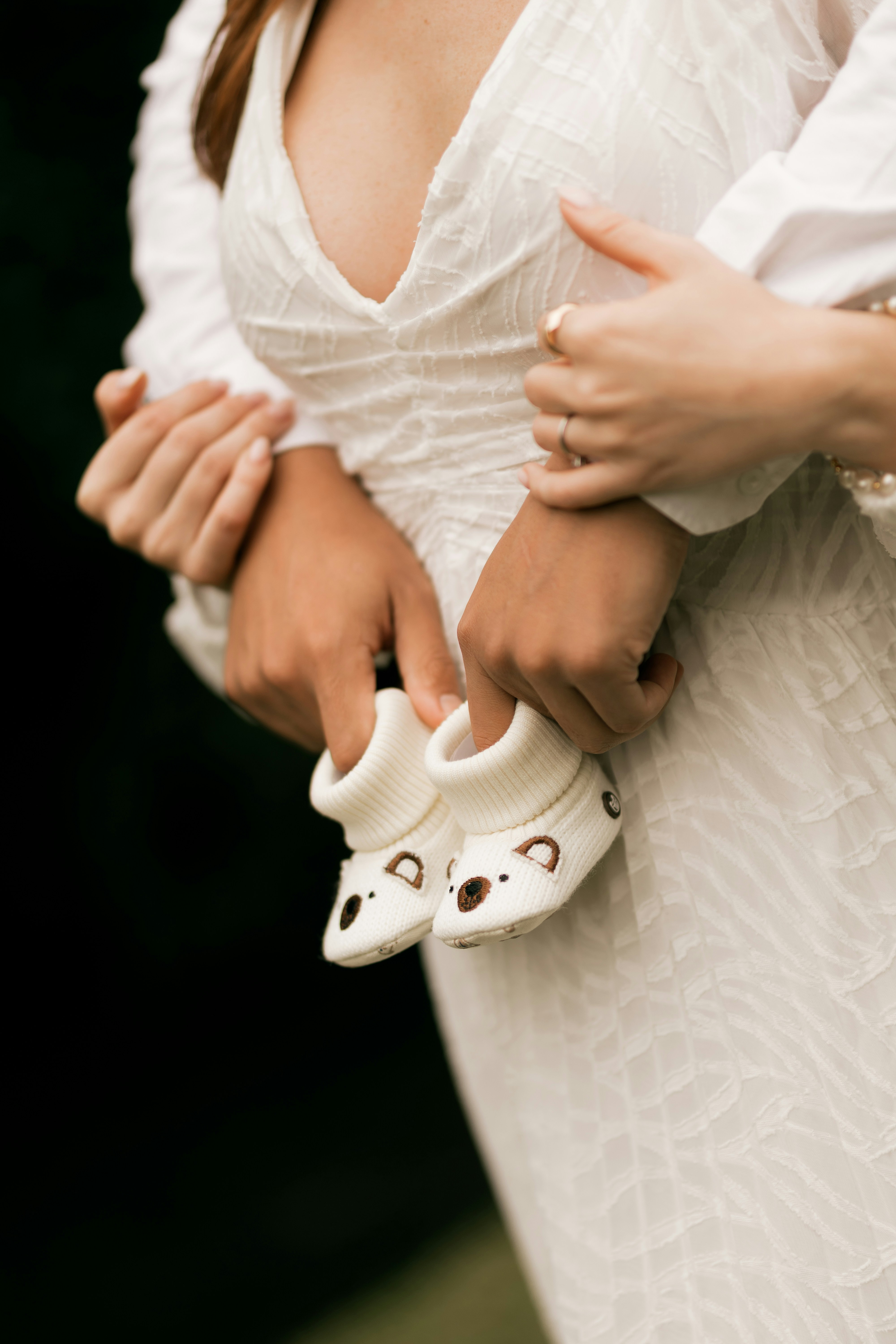 Tangan pasangan dengan lembut memegang sepatu bot bayi putih kecil.