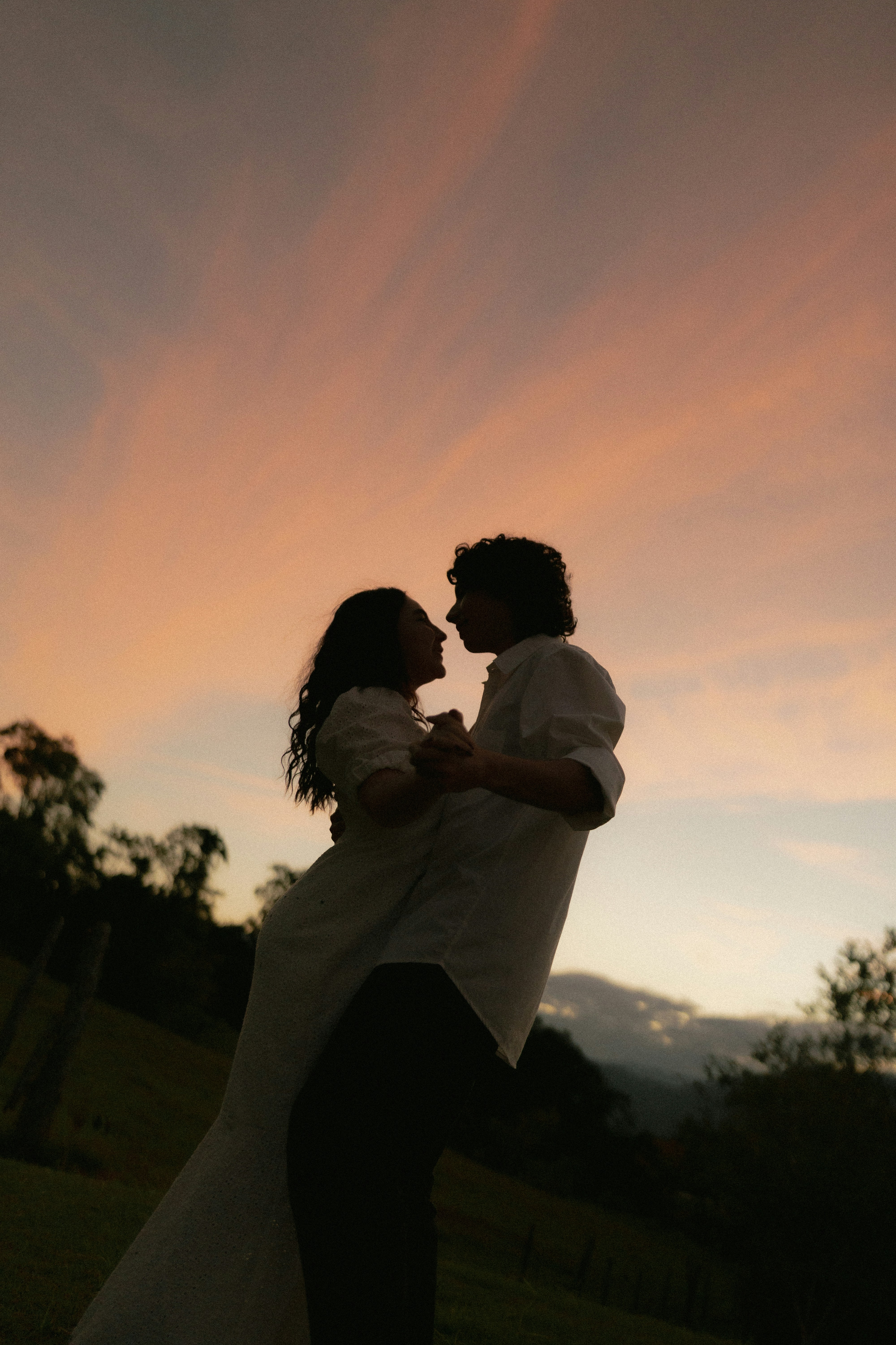 A couple embraces against a beautiful sunset sky.