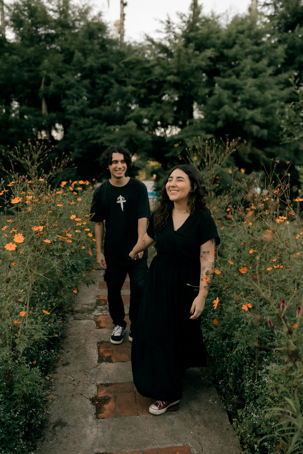 A smiling couple walking hand in hand along a flower-lined path together