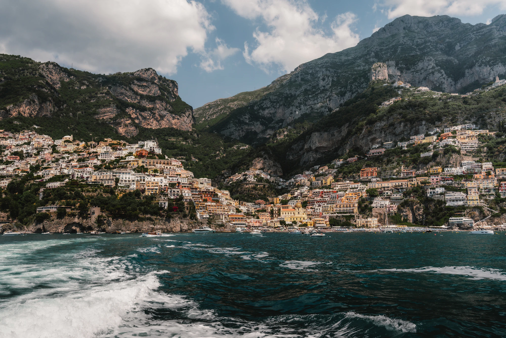 A cliffside town on the Amalfi coast under heavy cloud, surf breaking below.