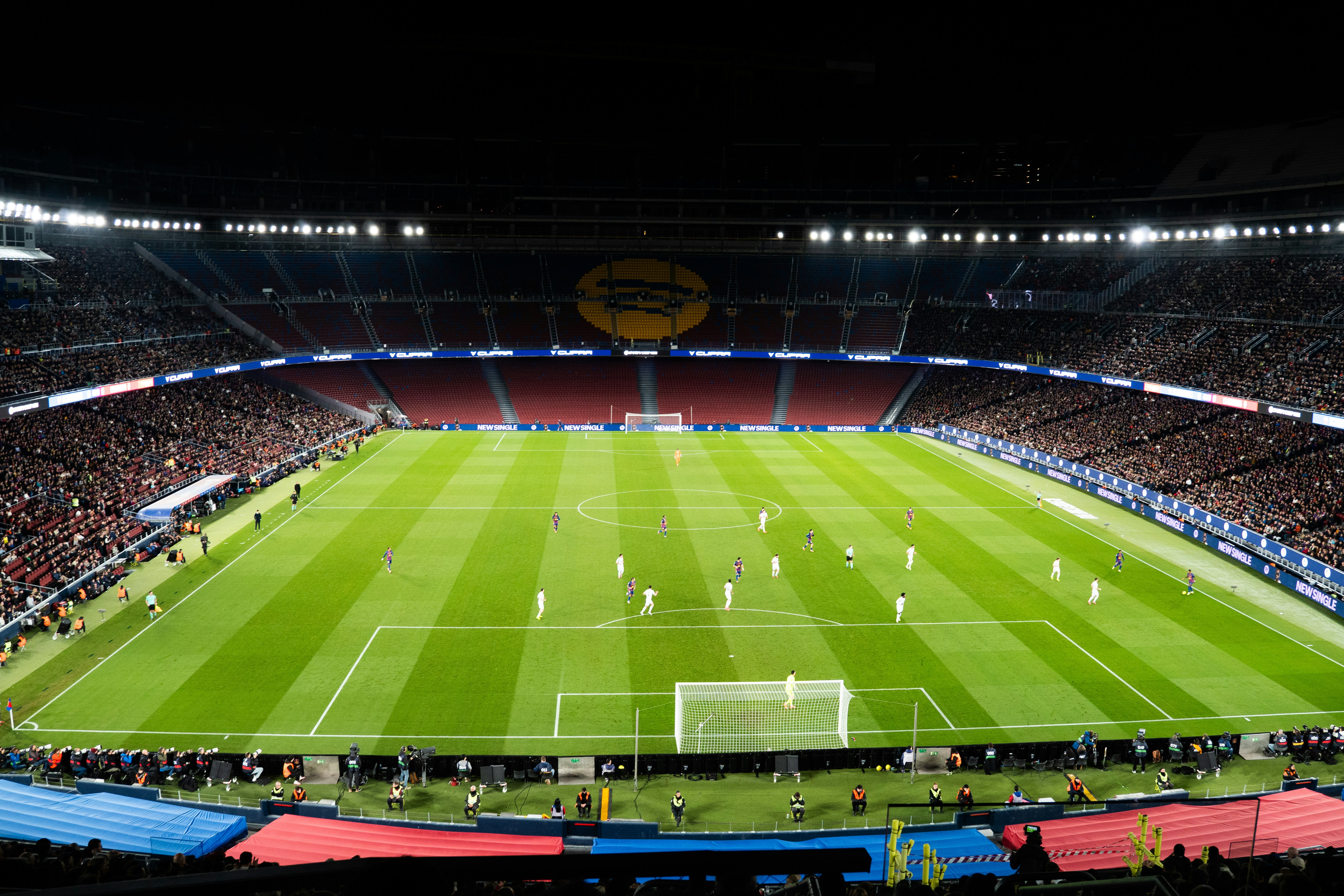 Pertandingan sepak bola di stadion yang terang benderang di malam hari.