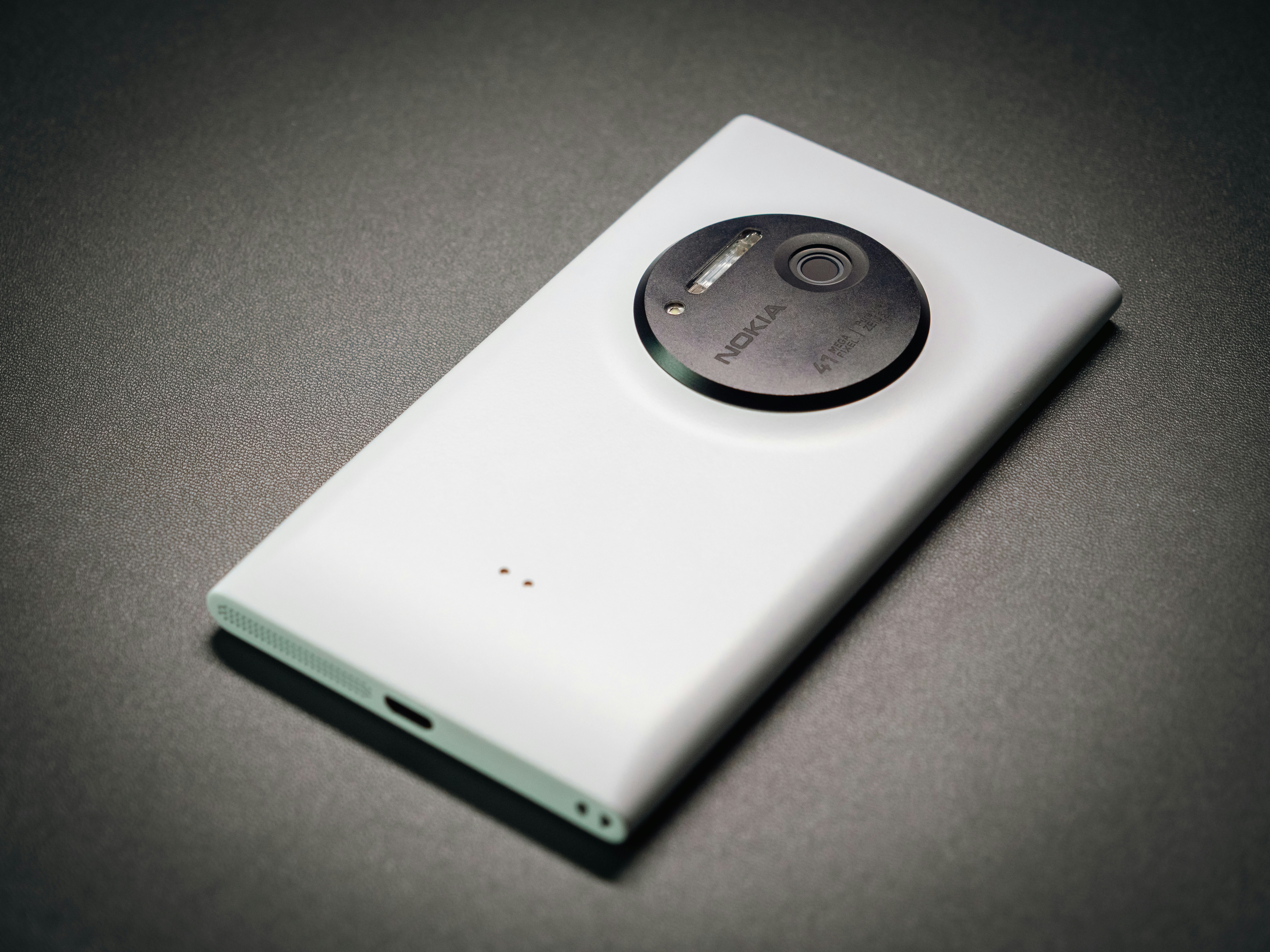 Smartphone blanc avec un grand objectif circulaire sur fond sombre.