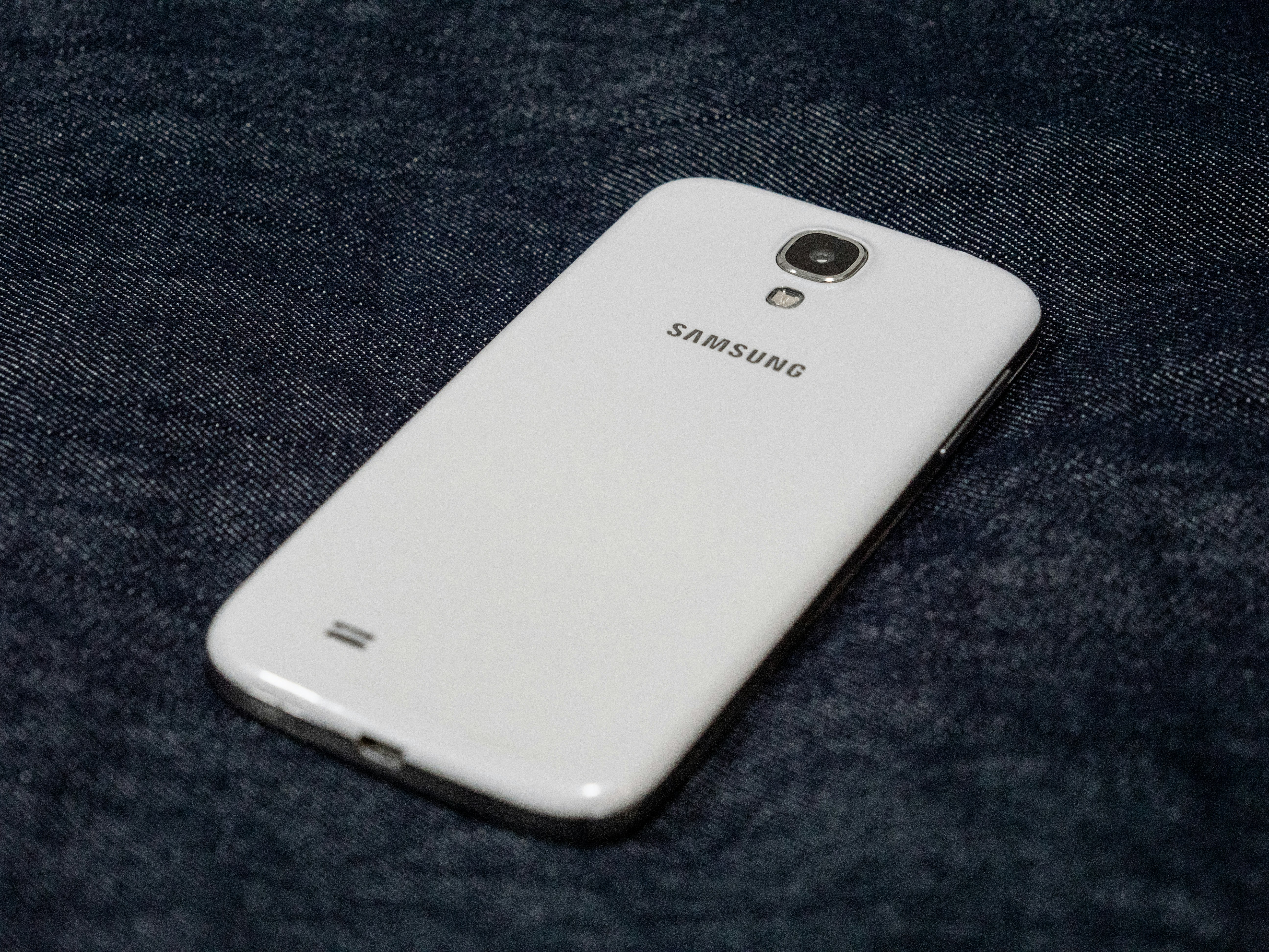 Un smartphone Samsung blanc repose sur une surface sombre et texturée.