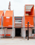 Modern building with orange box structures and scaffolding.
