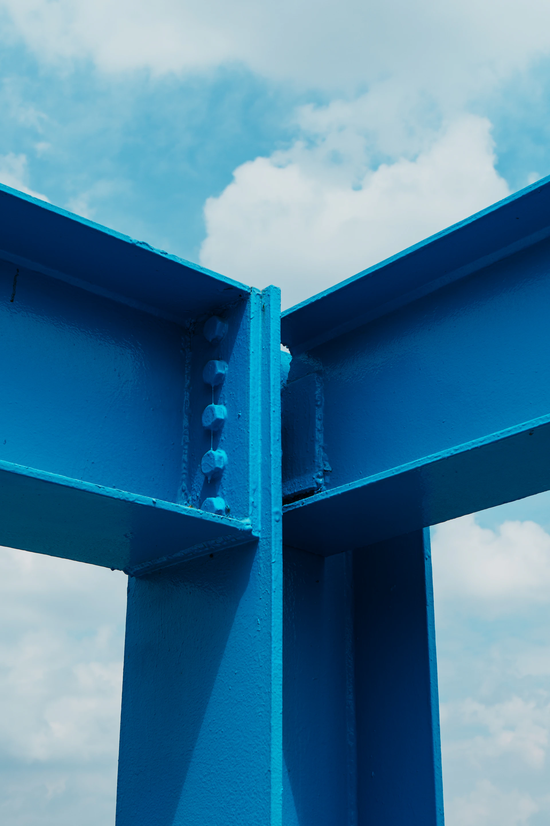 Bright blue structural steel beams against a cloudy sky.
