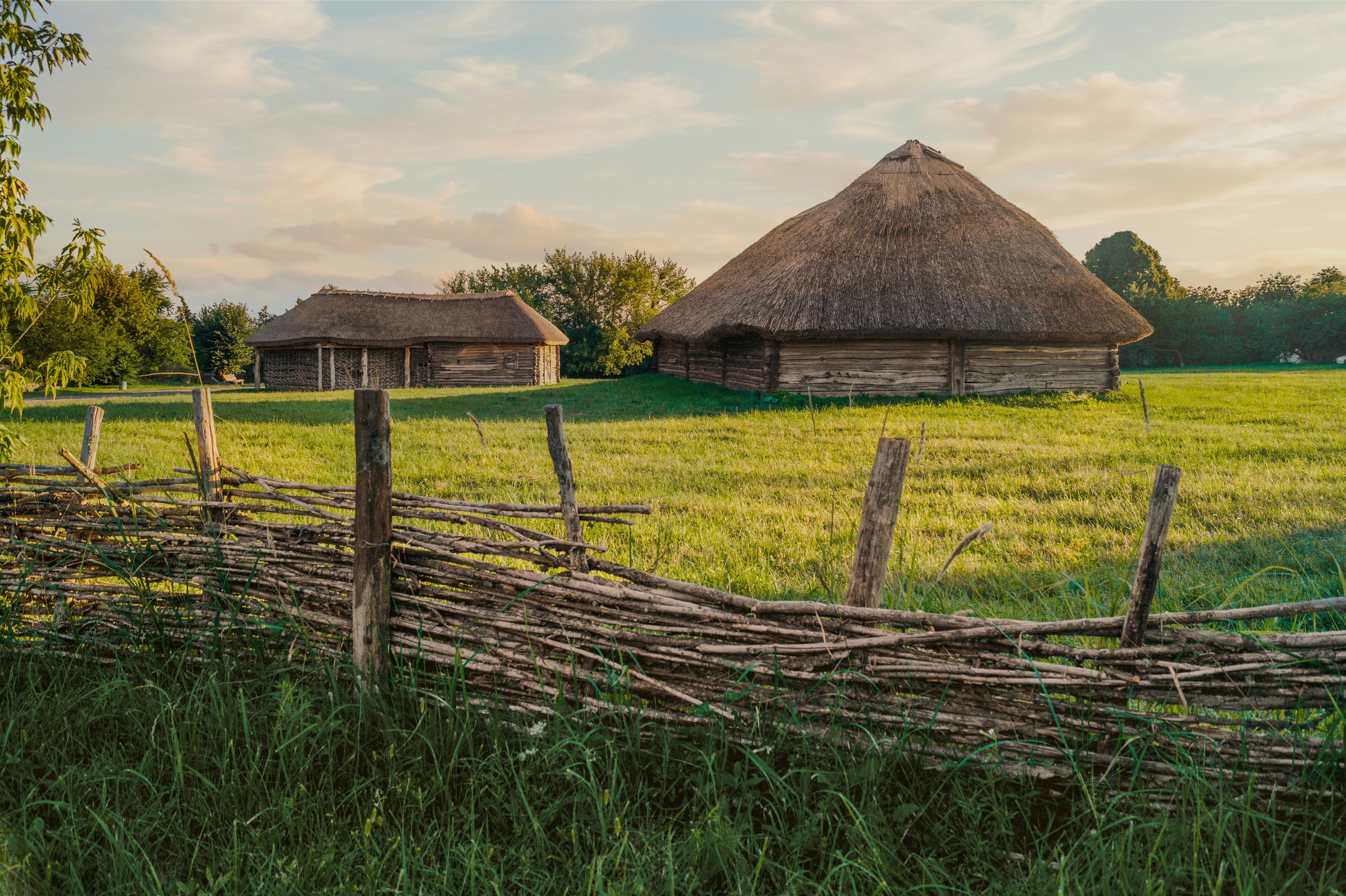 Rustikaler geflochtener Zaun auf einem Feld mit traditionellen Strohdächern.